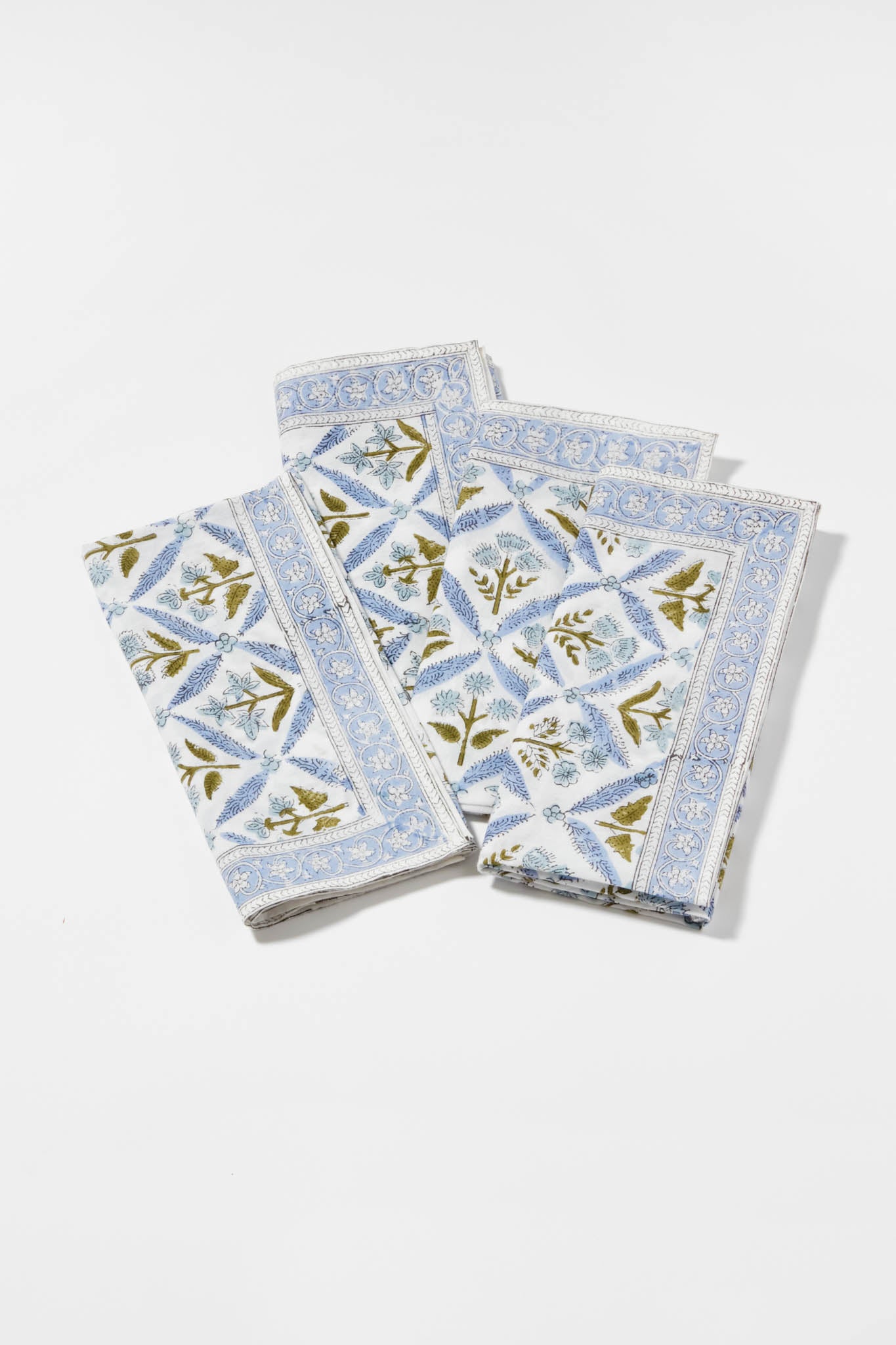 Three folded cotton napkins by Locust Walk feature a blue floral and geometric pattern, inspired by Hydrangea Blue Garden Trellis Napkins.