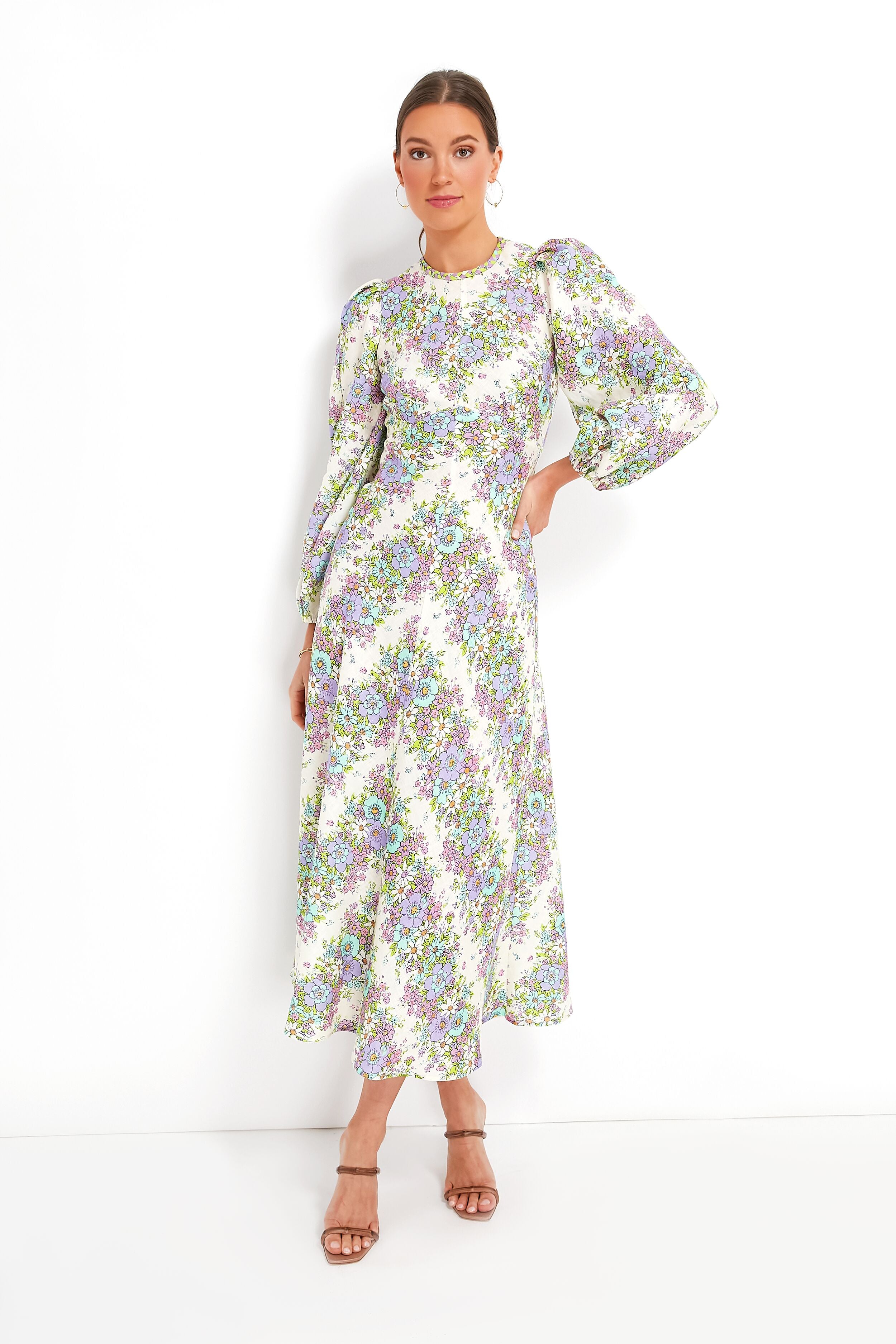 A woman wears an Alemais Petal Agnes Midi linen dress with a floral chevron print, puffed sleeves, and tan heeled sandals.