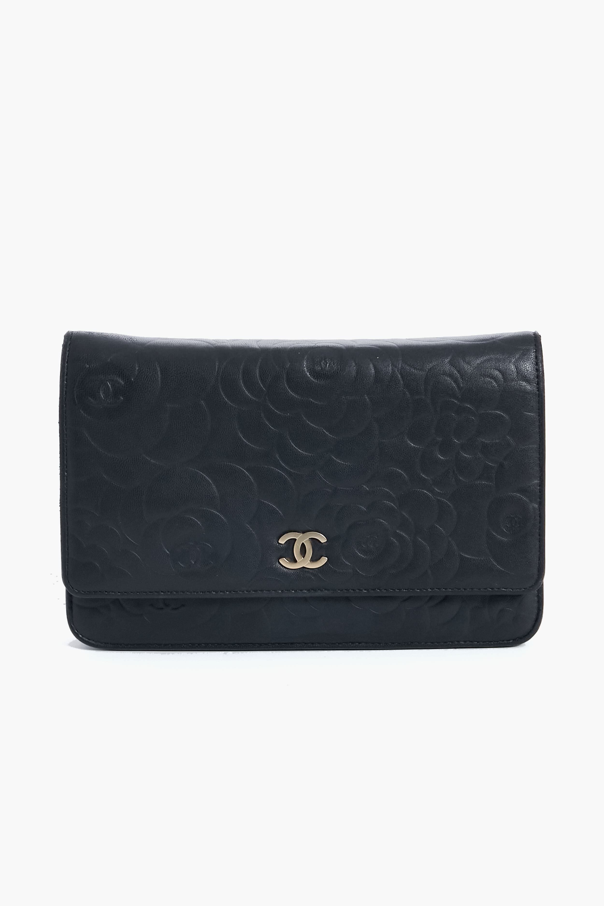 A black leather clutch from Tuckernuck Archive Collection featuring an embossed floral pattern and a gold logo on the front flap.