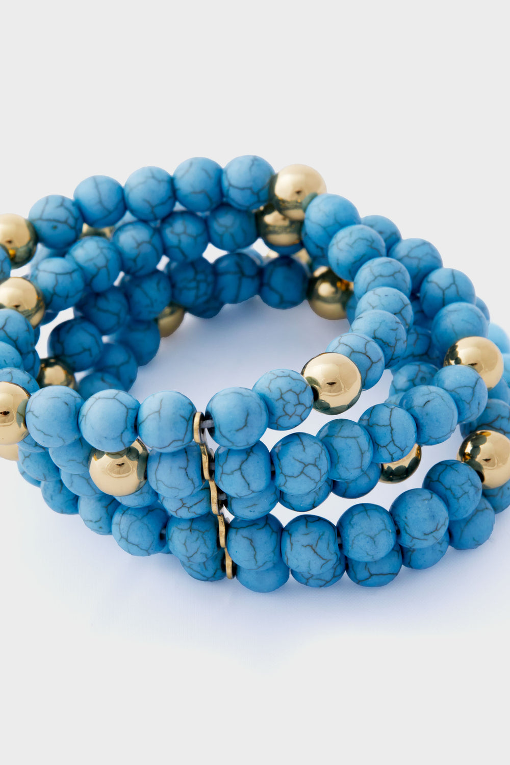 A coiled, stacked bracelet from Tuckernuck Jewelry featuring round turquoise beads with gold accents, arranged in multiple loops.
