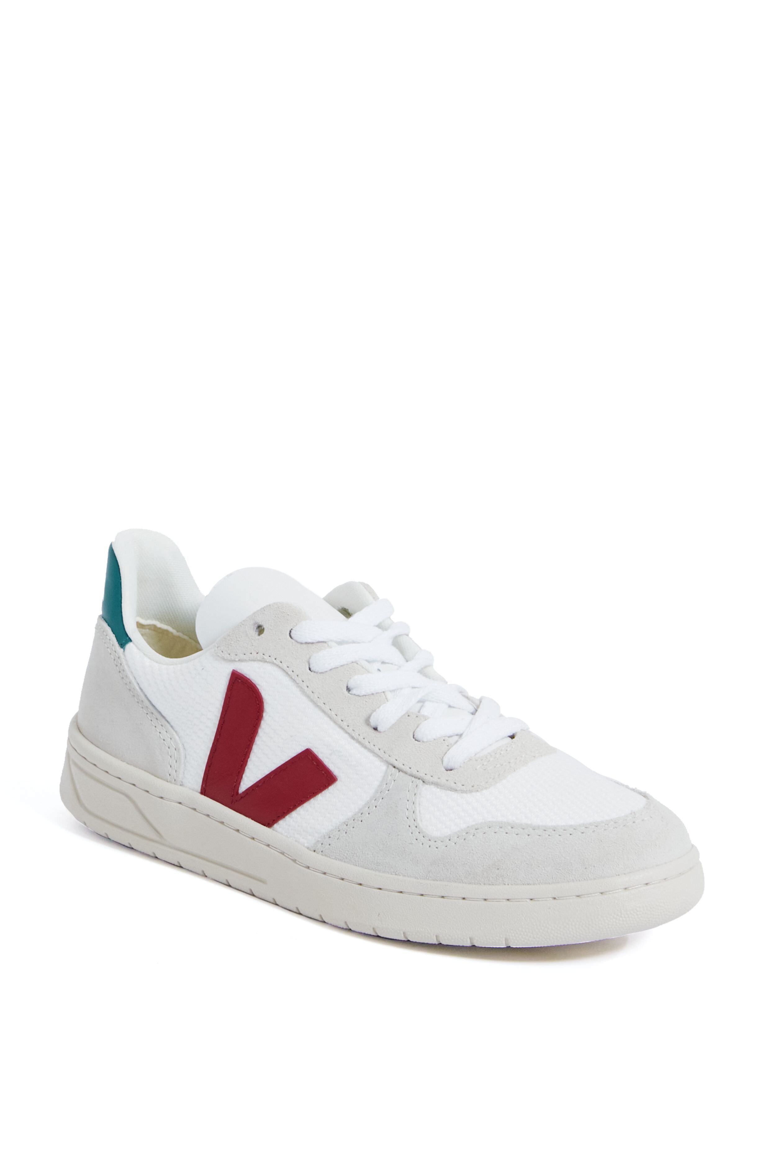The VEJA low-top sneaker features a white design with light gray suede accents, a red V logo on the side, and a teal heel patch, all crafted from eco-friendly materials.