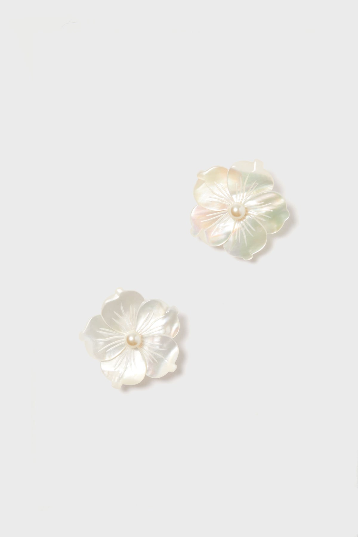 Jennifer Behr’s iridescent mother-of-pearl floral stud earrings, each with a pearl center, add a luxurious touch to any ensemble.