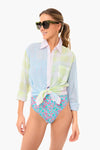 A woman stands confidently in Solid & Striped sunglasses, a light pastel plaid Long Oxford Tunic tied at the waist, and high-waisted floral swimwear bottoms.