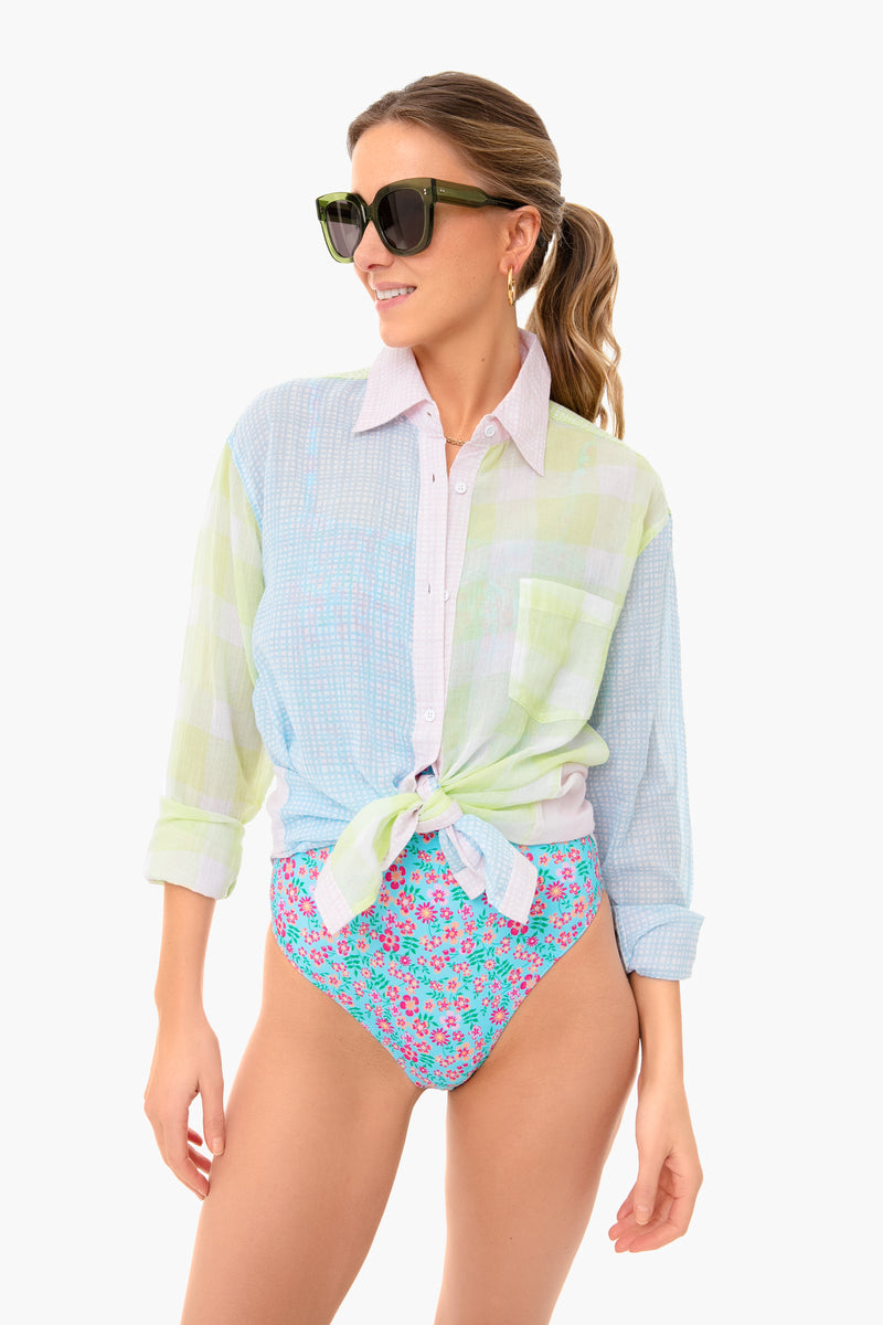A woman stands confidently in Solid & Striped sunglasses, a light pastel plaid Long Oxford Tunic tied at the waist, and high-waisted floral swimwear bottoms.