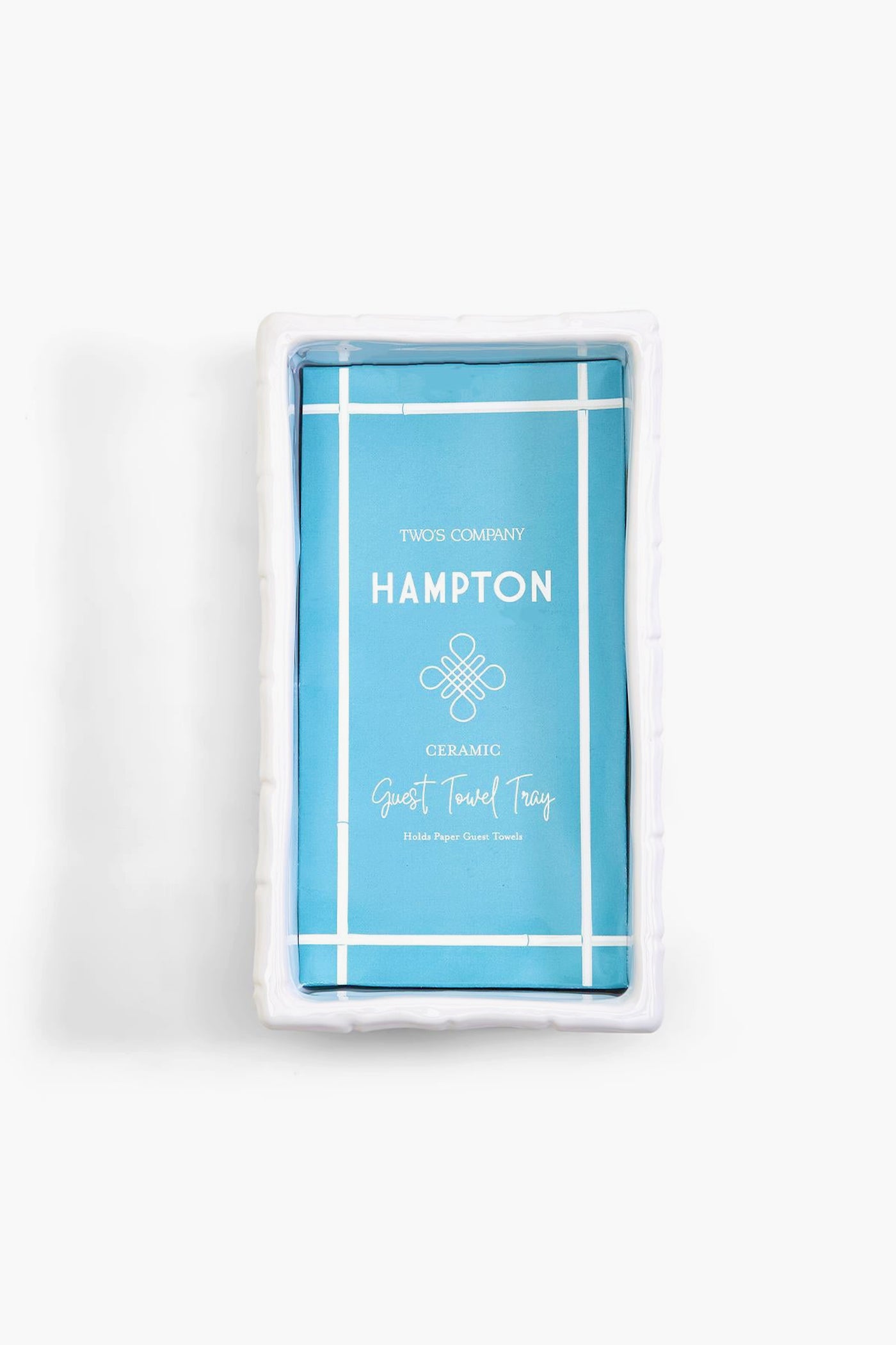 A white rectangular ceramic tray in chinoiserie style holds a blue package labeled "Hampton Guest Towel Tray" by Two's Company.