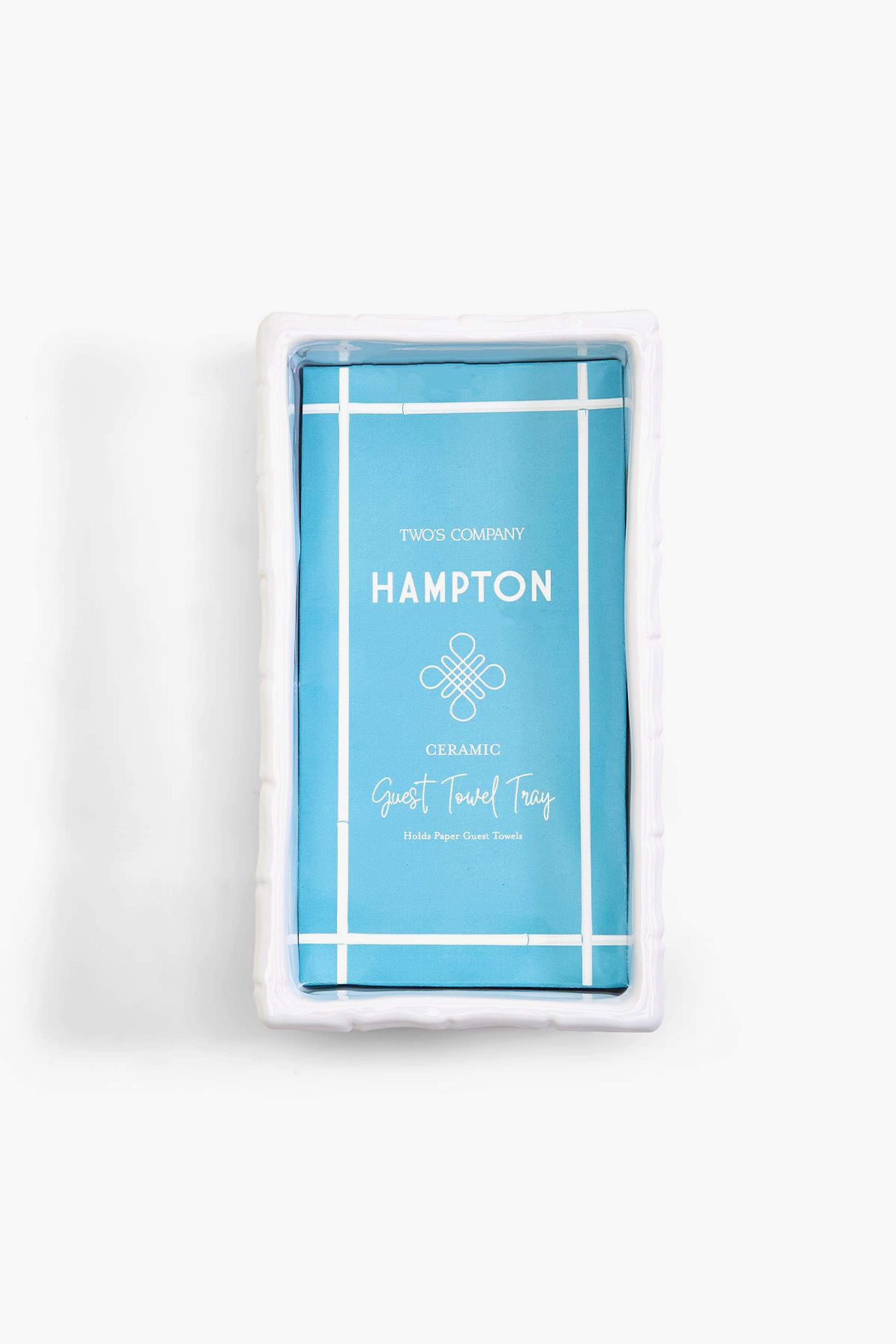 A white rectangular ceramic tray in chinoiserie style holds a blue package labeled "Hampton Guest Towel Tray" by Two's Company.