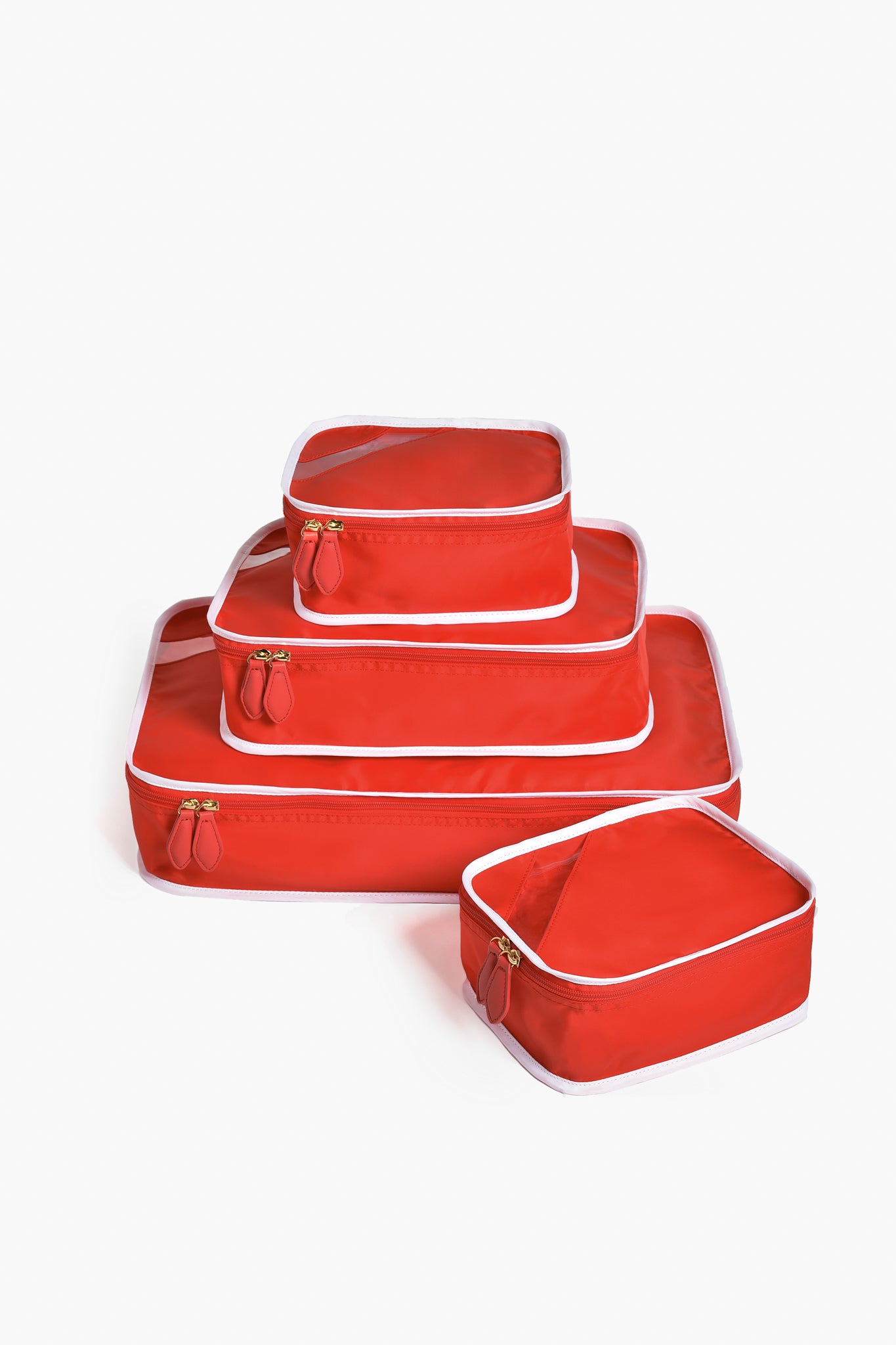 Four red Paravel packing cubes with white trim, stacked by size, provide a stylish and sustainable travel storage organizer for your luggage.