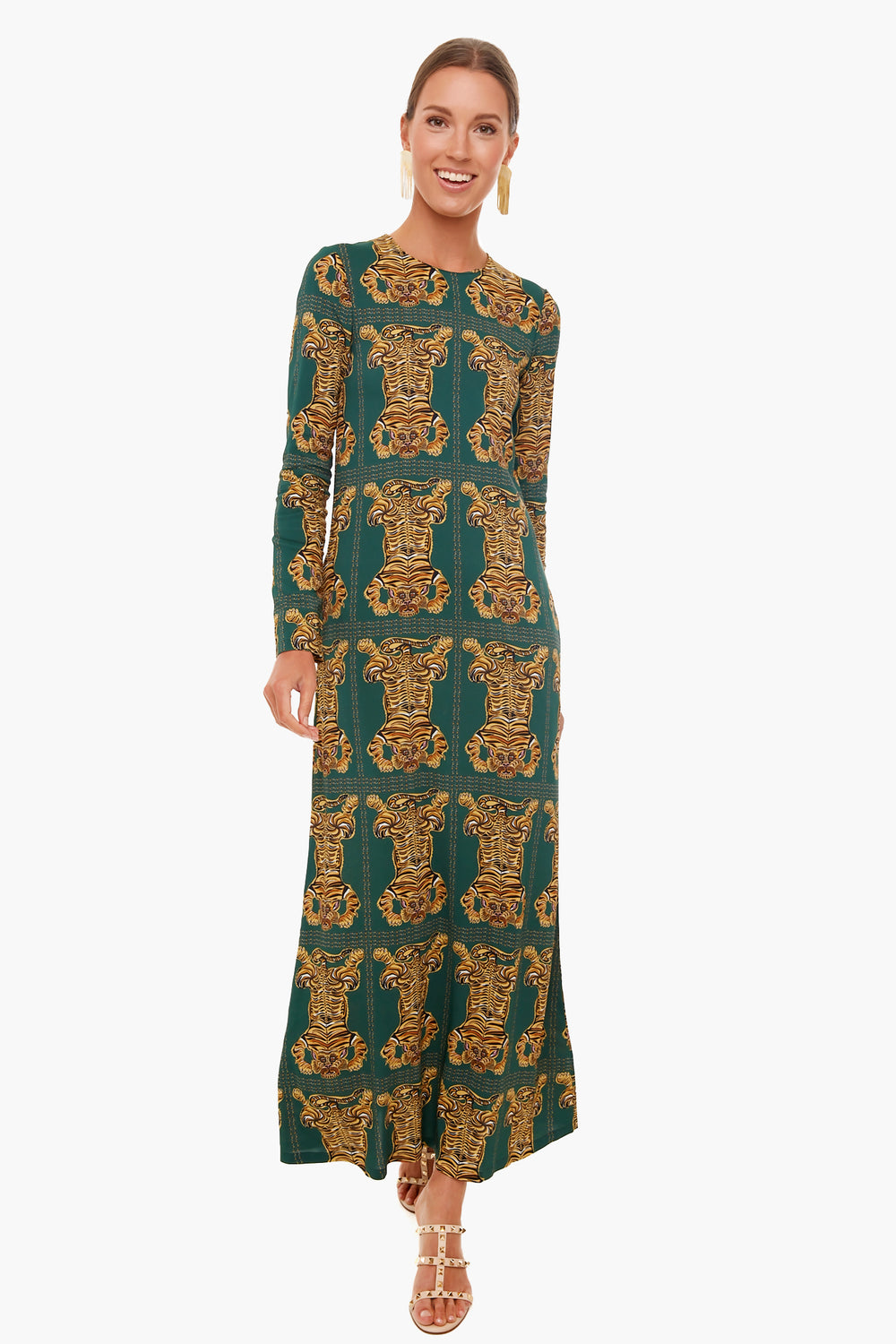 Woman wearing a green La DoubleJ long-sleeve swing dress with gold ornate patterns, paired with gold earrings and strappy sandals, standing and smiling.