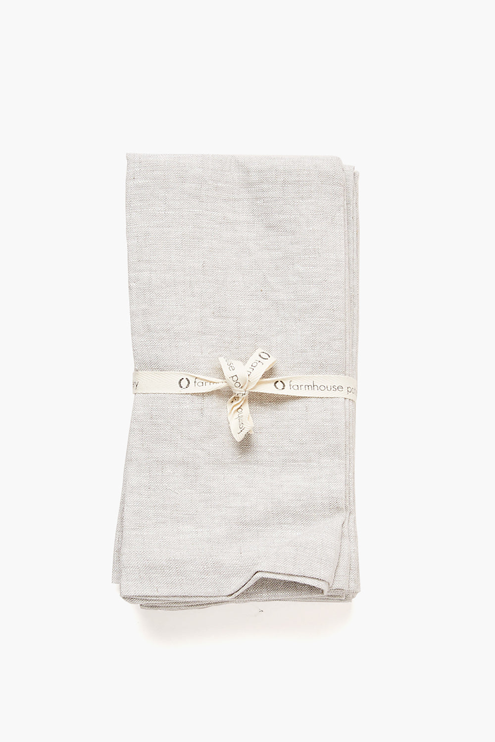 A neatly folded light gray Stone Washed Linen Napkin from Farmhouse Pottery, Inc is tied with a cream-colored ribbon labeled Farmhouse Pottery.