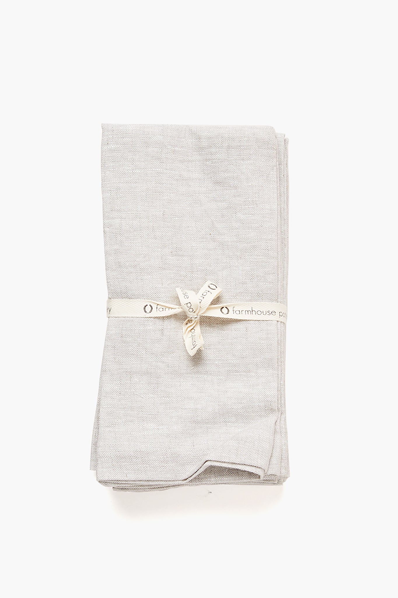 A neatly folded light gray Stone Washed Linen Napkin from Farmhouse Pottery, Inc is tied with a cream-colored ribbon labeled Farmhouse Pottery.