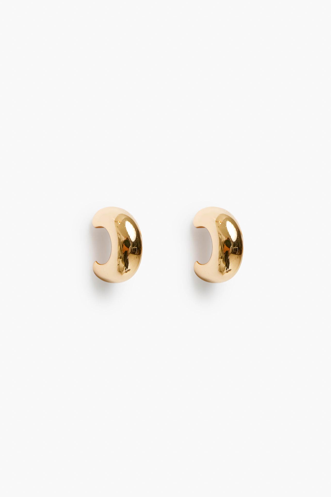 A pair of small, polished 18k gold plated ear cuffs with a smooth, curved design from Petit Moments, a woman-owned brand.