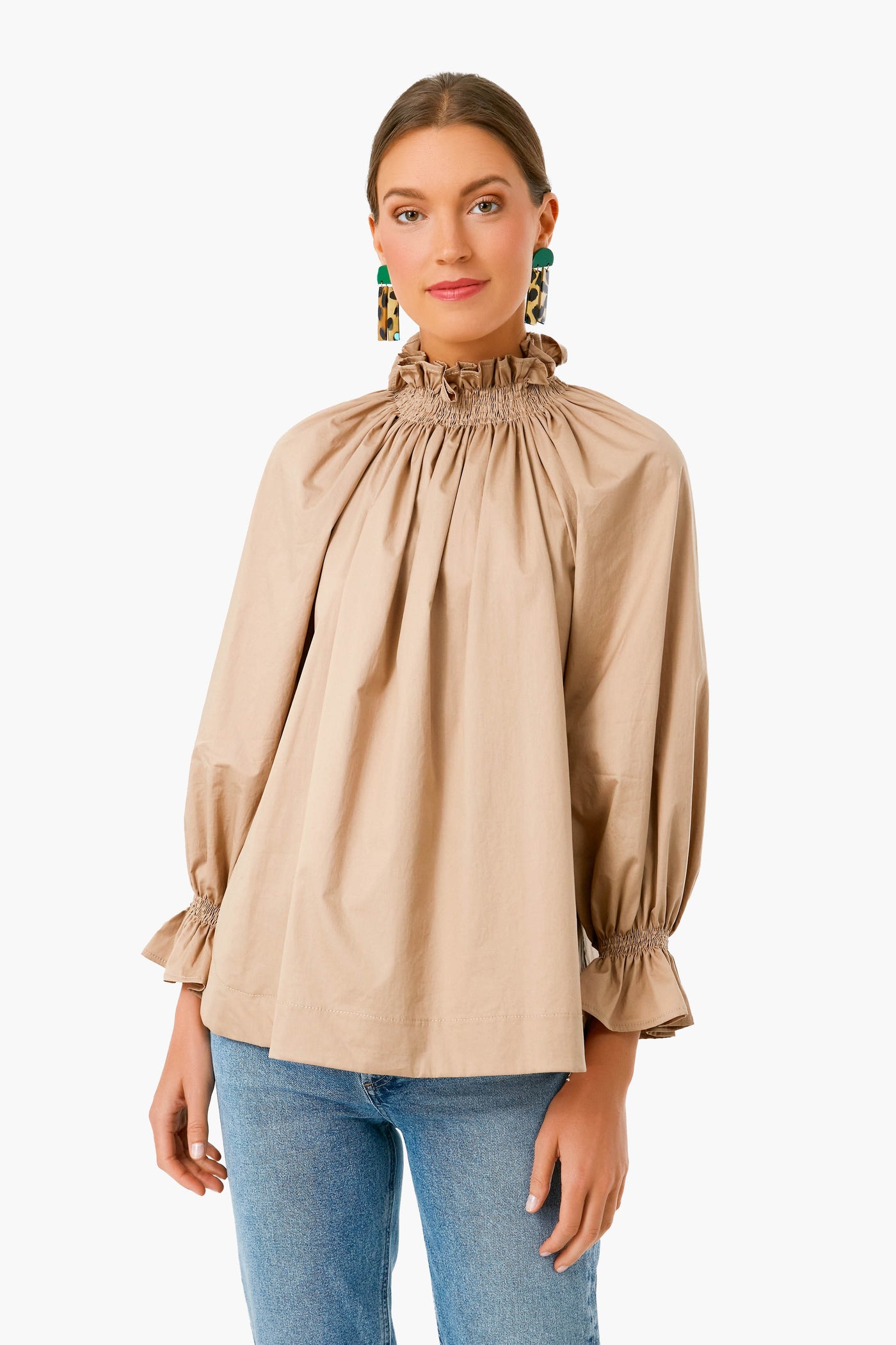 Monica Nera woman in a beige long sleeve top with ruffled neckline and cuffs, paired with blue jeans—crafted from eco-cotton for a sustainable fashion statement.