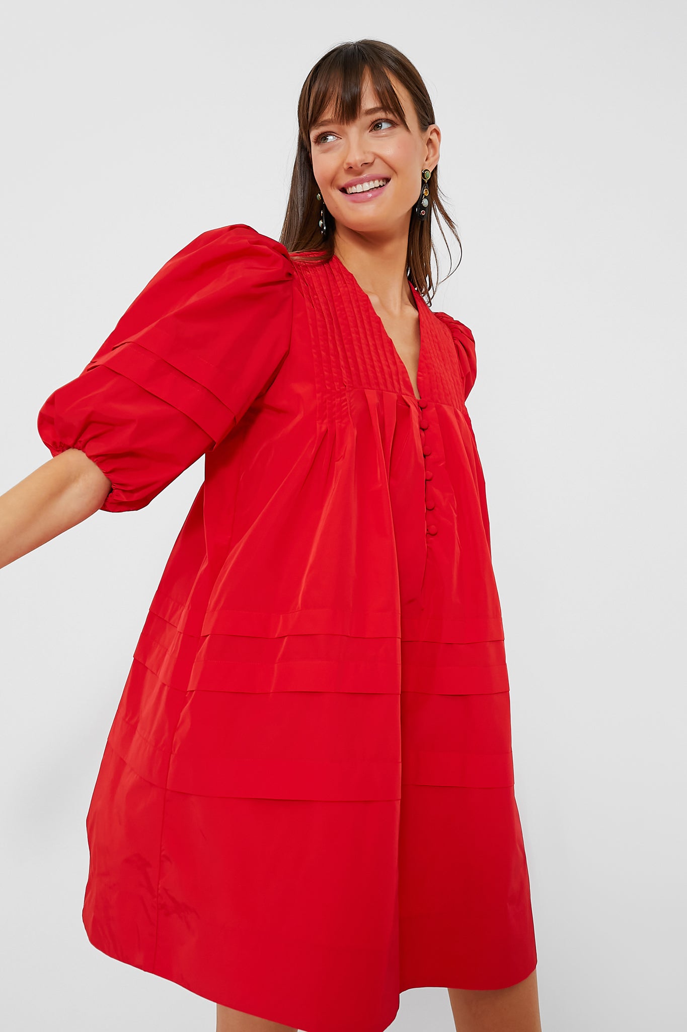 A woman stands confidently in the Hunter Bell Scarlet Jenkins mini dress, a loose-fitting, bright red style with puffed half sleeves.