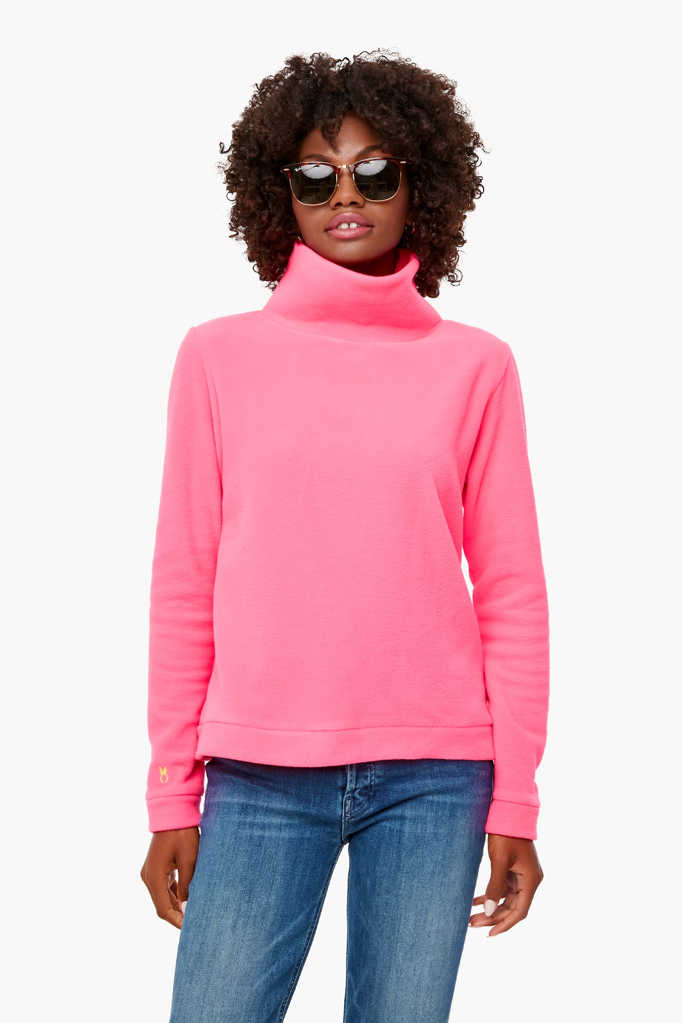 A woman wearing a Dudley Stephens Neon Pink Park Slope funnel neck fleece made from sustainable recycled yarn, paired with blue jeans and sunglasses.