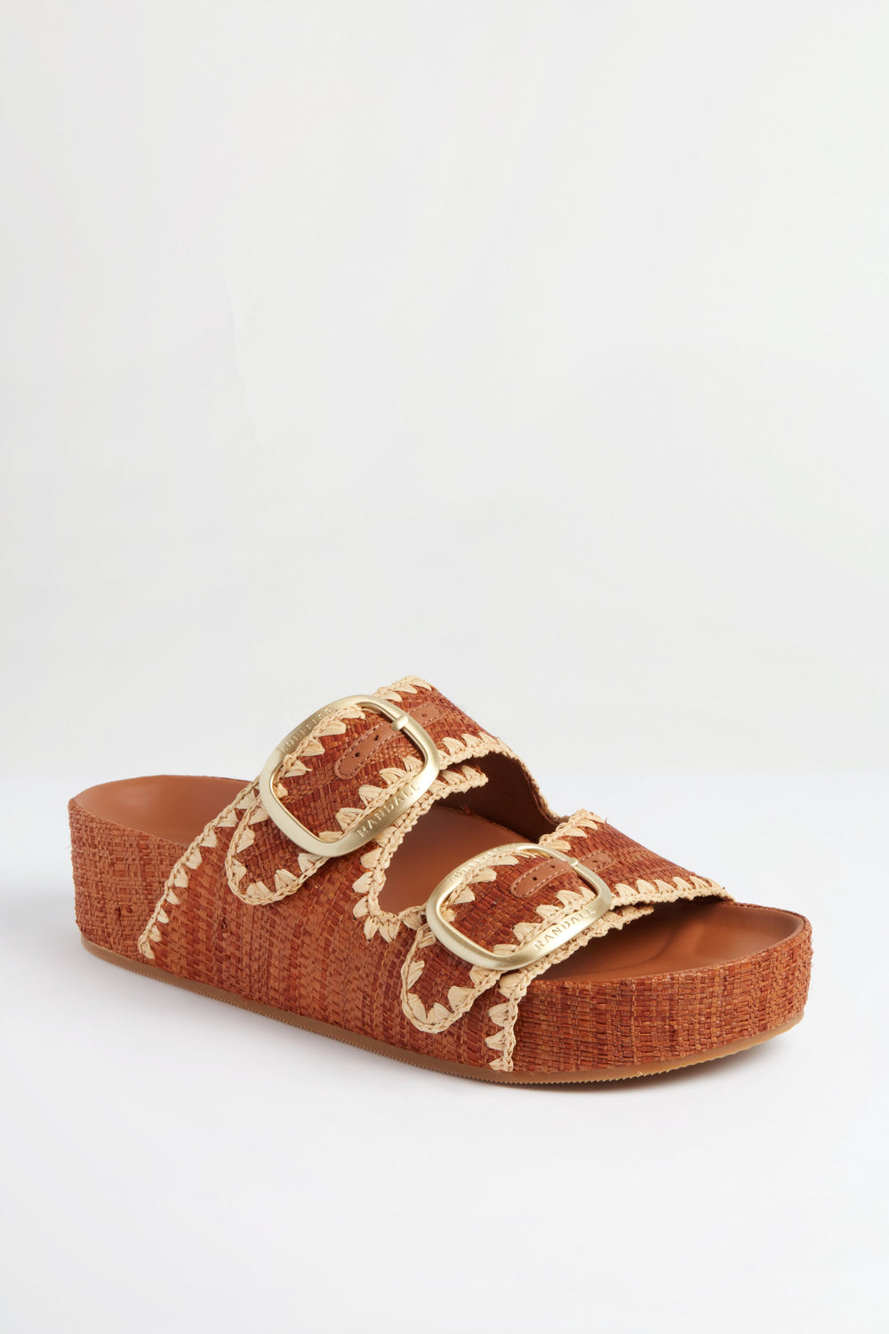 A brown platform slide sandal by Loeffler Randall, featuring two large gold buckles and cream stitching, inspired by the Brown Straw Theo Sandal.