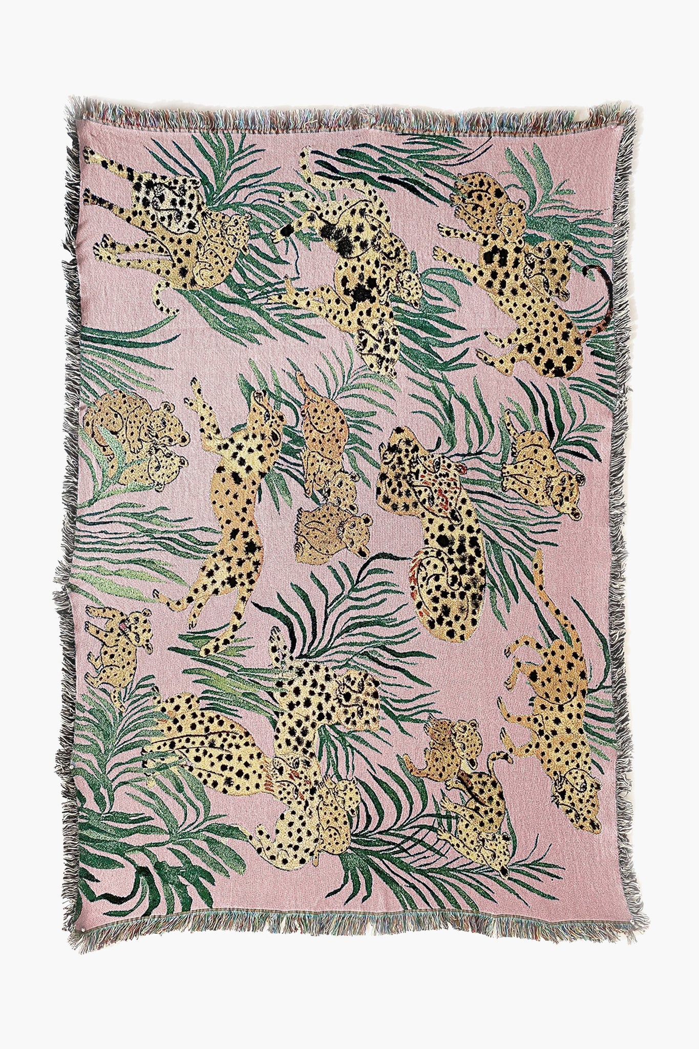 The Olivia Wendel Pink Cheetahs Blanket features spotted leopards and green leaves on a pink background, finished with a fringe. Made from 100% US-grown cotton, it adds a playful accent to any room.