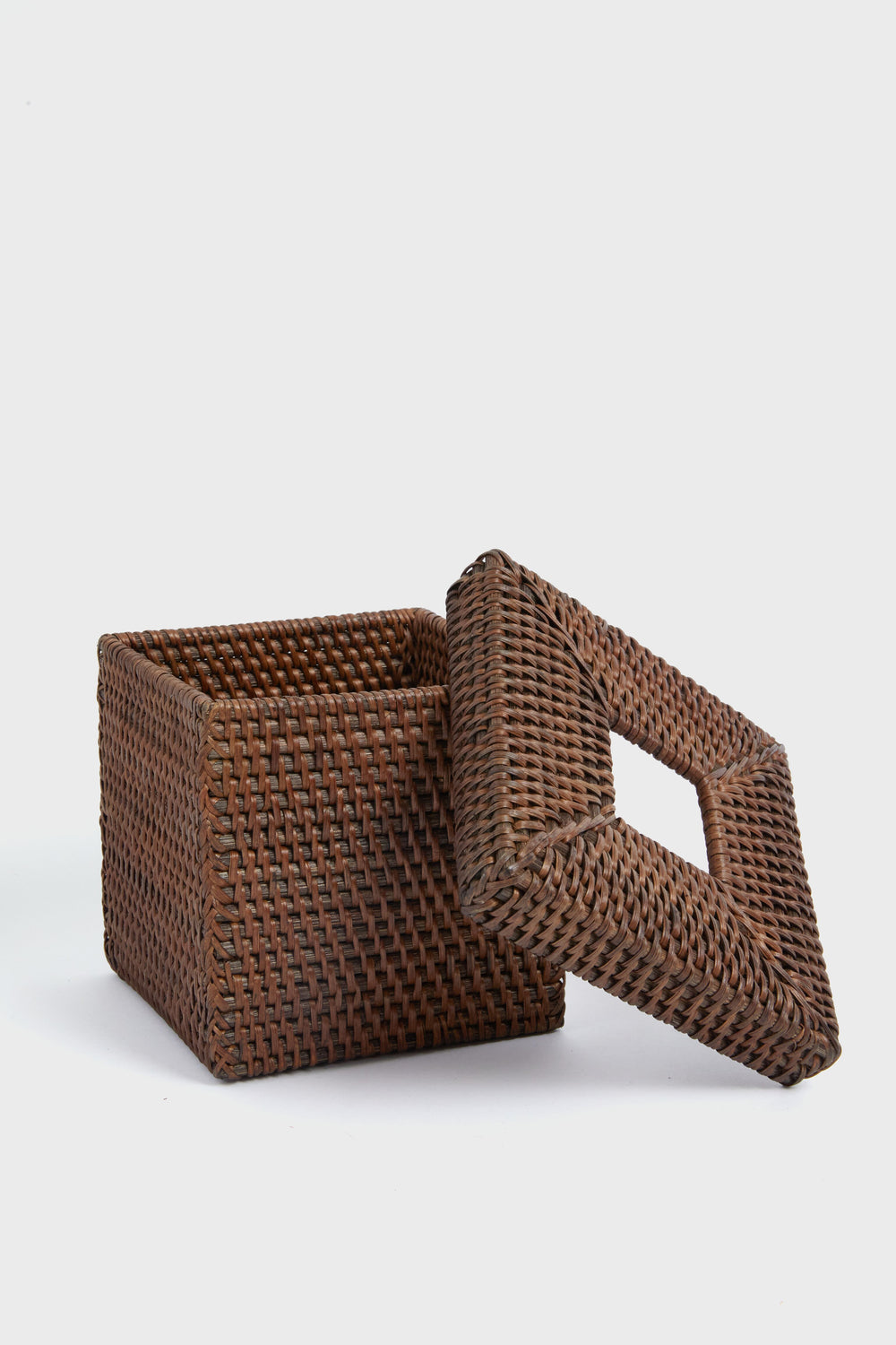 A square, brown woven tissue box cover with matching lid from Tuckernuck Home rests nearby, crafted in a decorative rattan style.