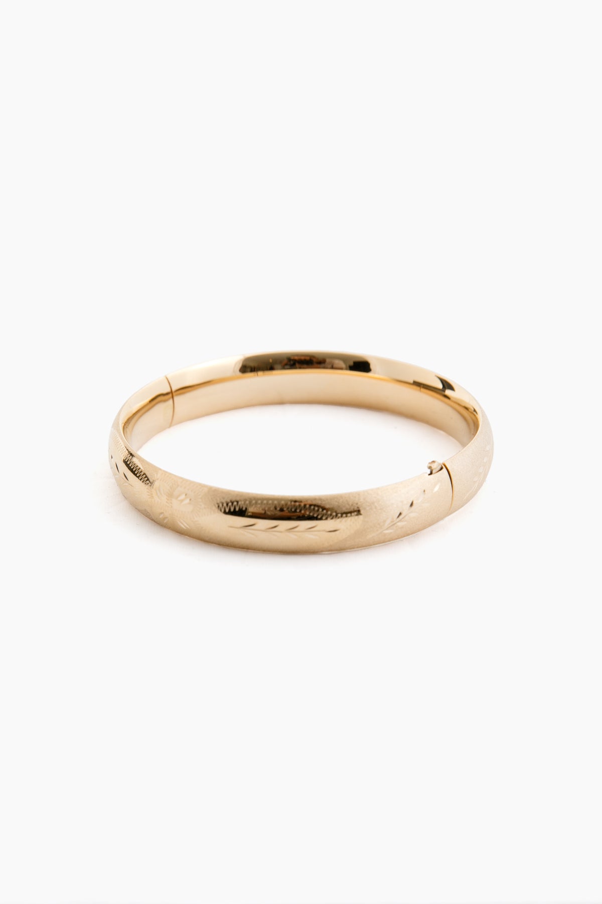 A plain 14K gold bangle bracelet by Tuckernuck Fine Jewelry, featuring a smooth, slightly rounded surface with a subtle etched floral pattern.