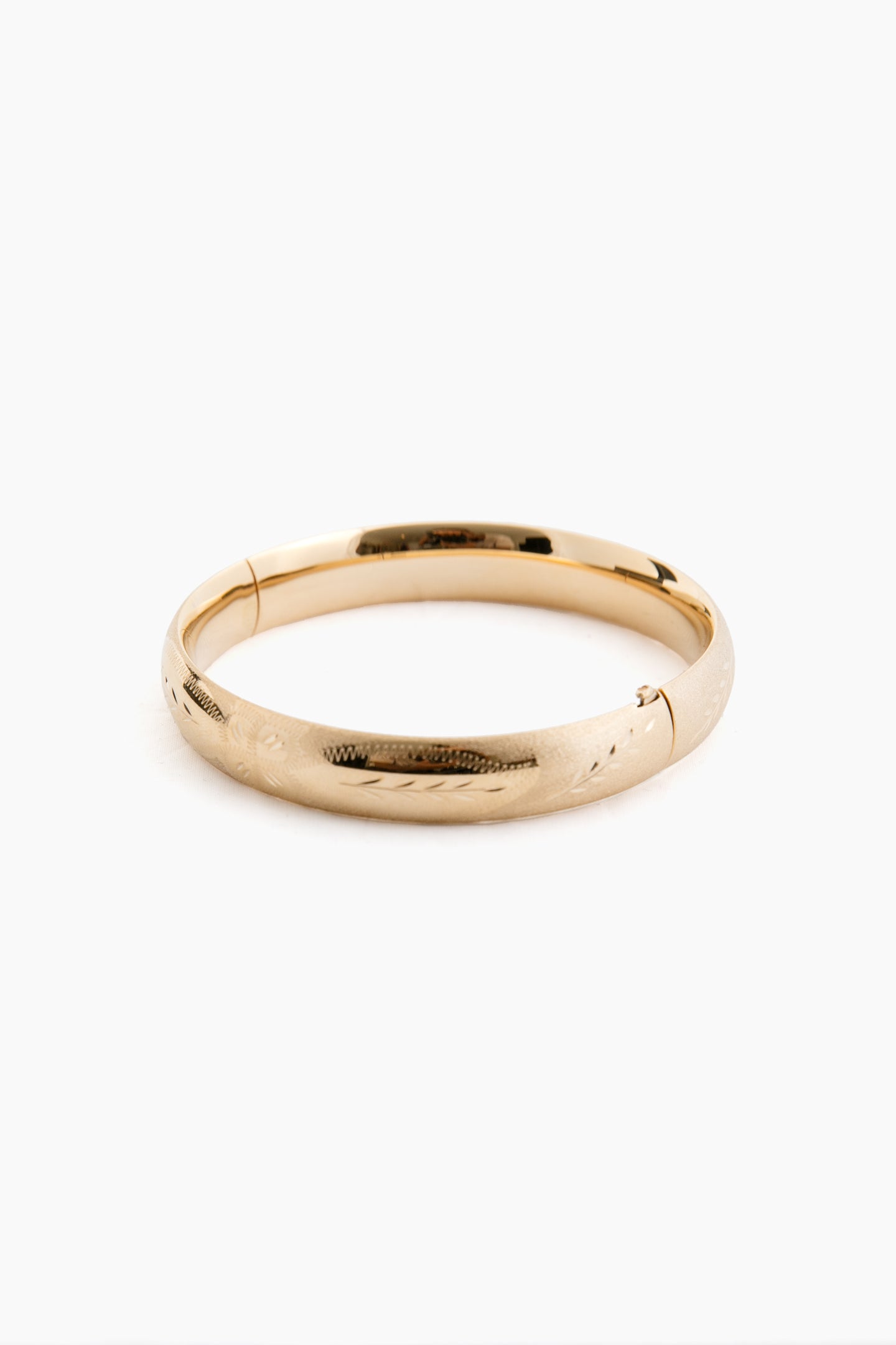 A plain 14K gold bangle bracelet by Tuckernuck Fine Jewelry, featuring a smooth, slightly rounded surface with a subtle etched floral pattern.