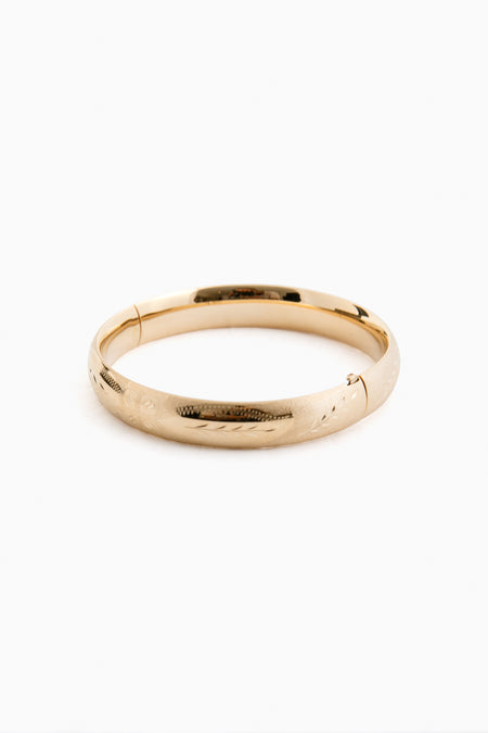 A plain 14K gold bangle bracelet by Tuckernuck Fine Jewelry, featuring a smooth, slightly rounded surface with a subtle etched floral pattern.