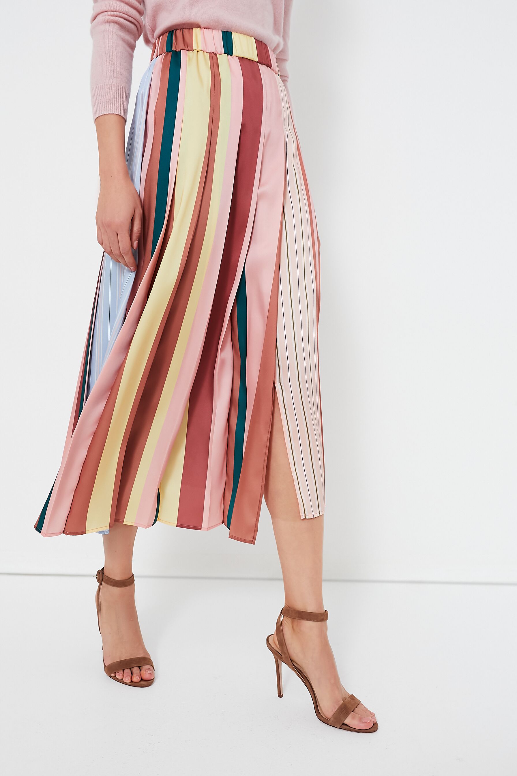 A person wears a pastel pink sweater, a pleated midi skirt by Weekend Max Mara in colorful hues, and tan high-heeled sandals.