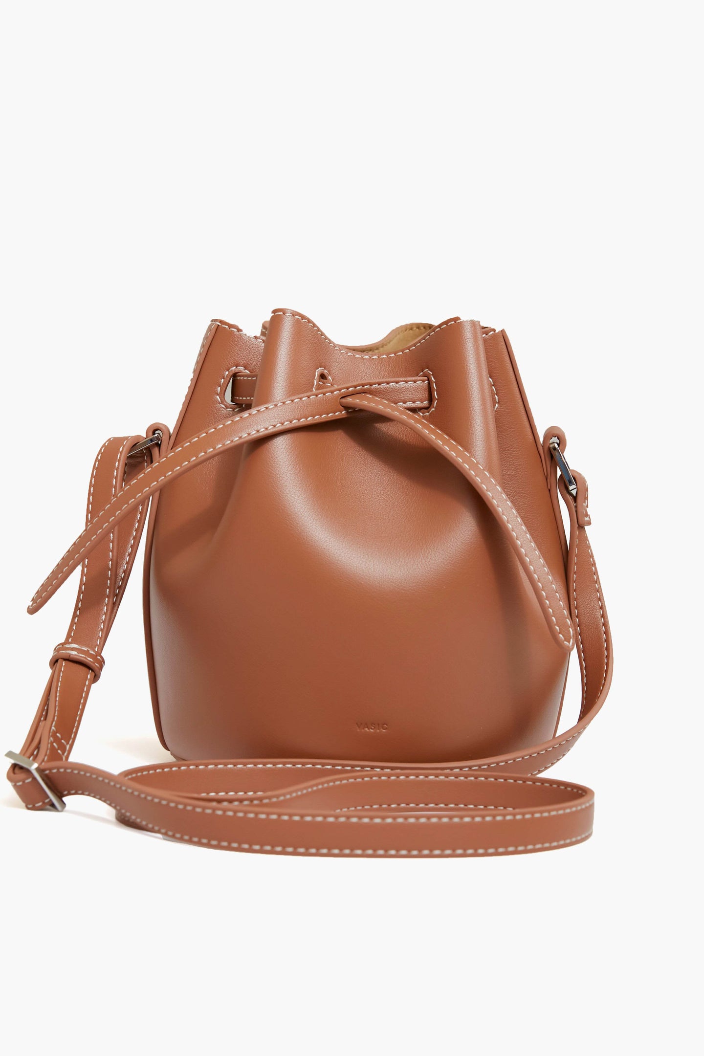 Vasic brown leather bucket bag featuring white stitching, an adjustable shoulder strap, smooth finish, and a drawstring closure.