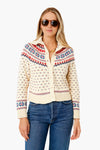 A woman stands confidently wearing THE GREAT. cream floral mini collar cardigan with red and blue designs, paired with blue jeans and sunglasses.