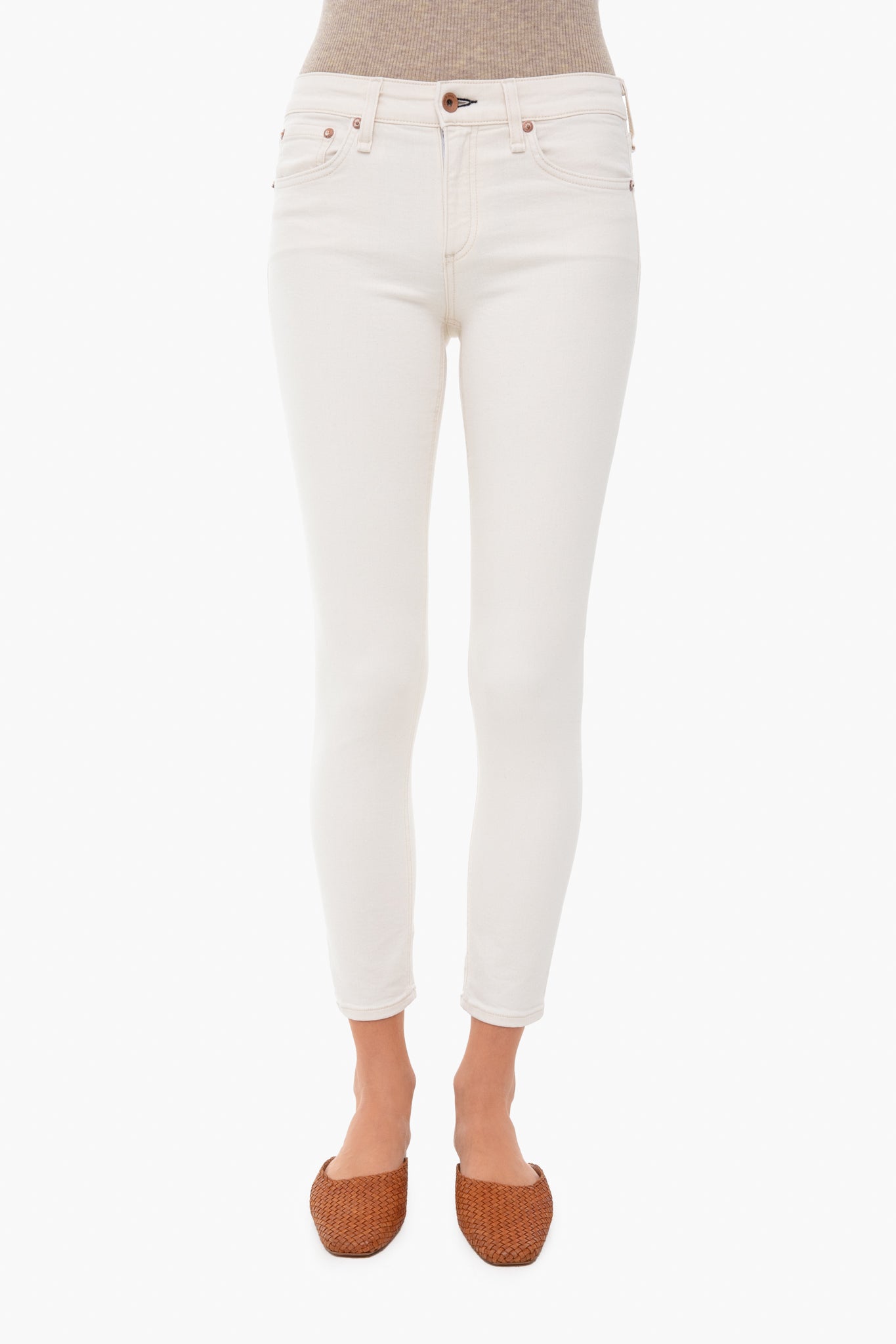 Sporting rag & bone light wash mid-rise ankle skinny jeans, a beige top, and brown woven flats, the person is photographed from waist to feet.
