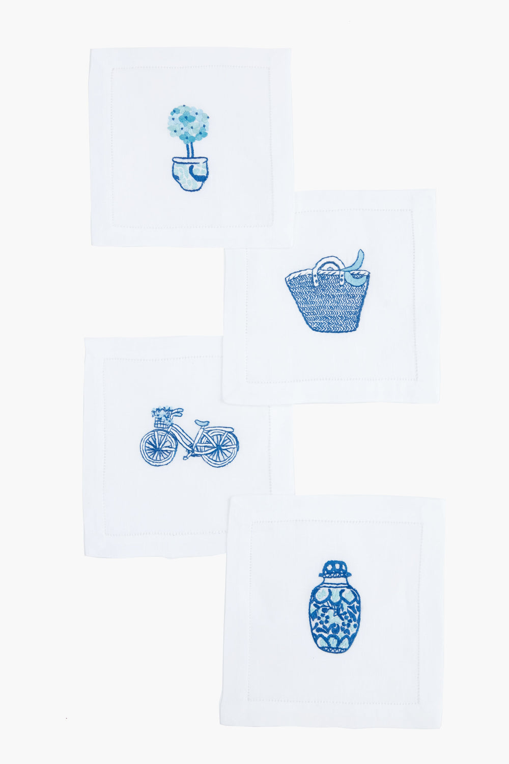 Set of four white linen hemstitch napkins by Tuckernuck Home, each with blue embroidery—a potted plant, basket, bicycle, and patterned vase—perfect as a hostess gift or for charming cocktail parties.