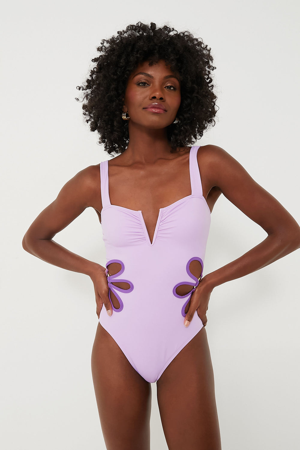 A woman wears a lavender bohemian one-piece swimsuit by follow suit, featuring a V-neckline and side cut-out flower designs, crafted from sustainable materials.