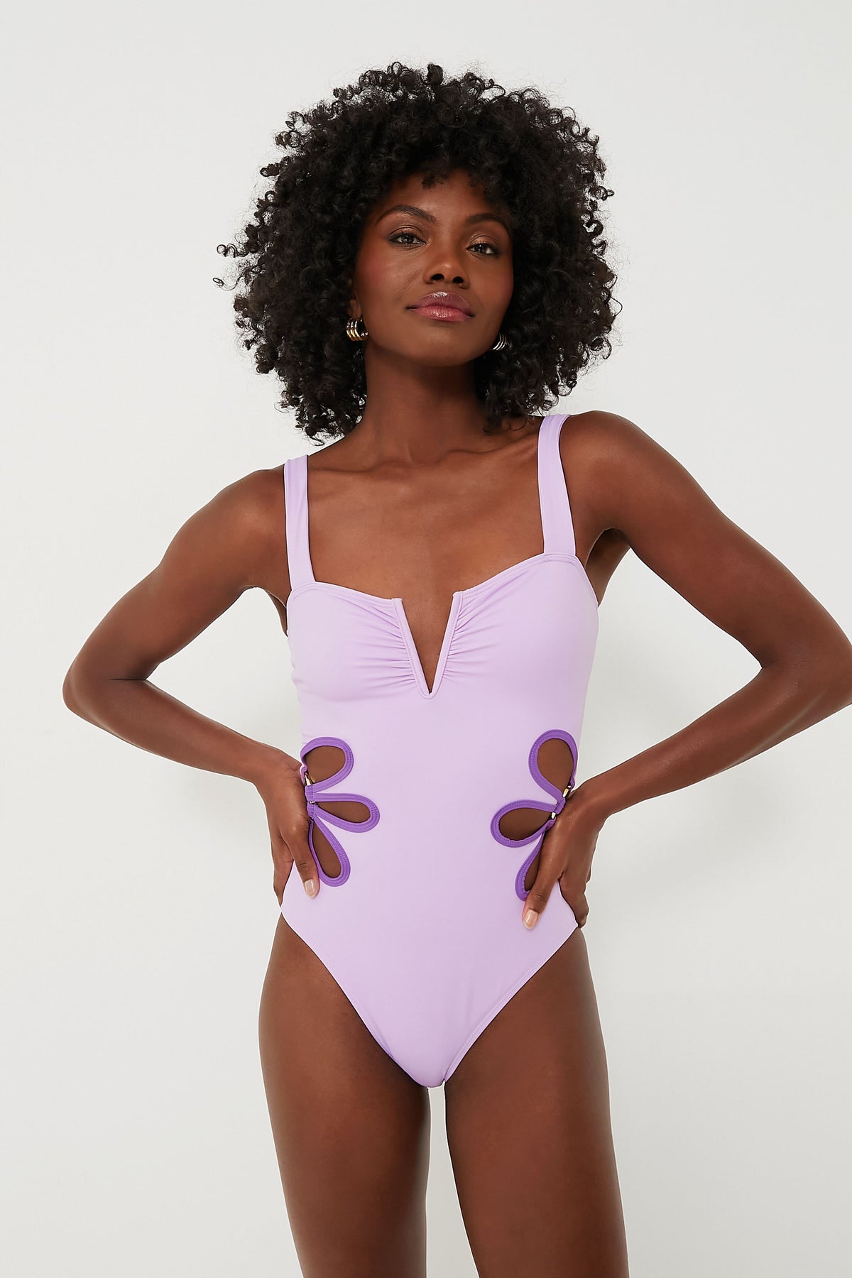 A woman wears a lavender bohemian one-piece swimsuit by follow suit, featuring a V-neckline and side cut-out flower designs, crafted from sustainable materials.