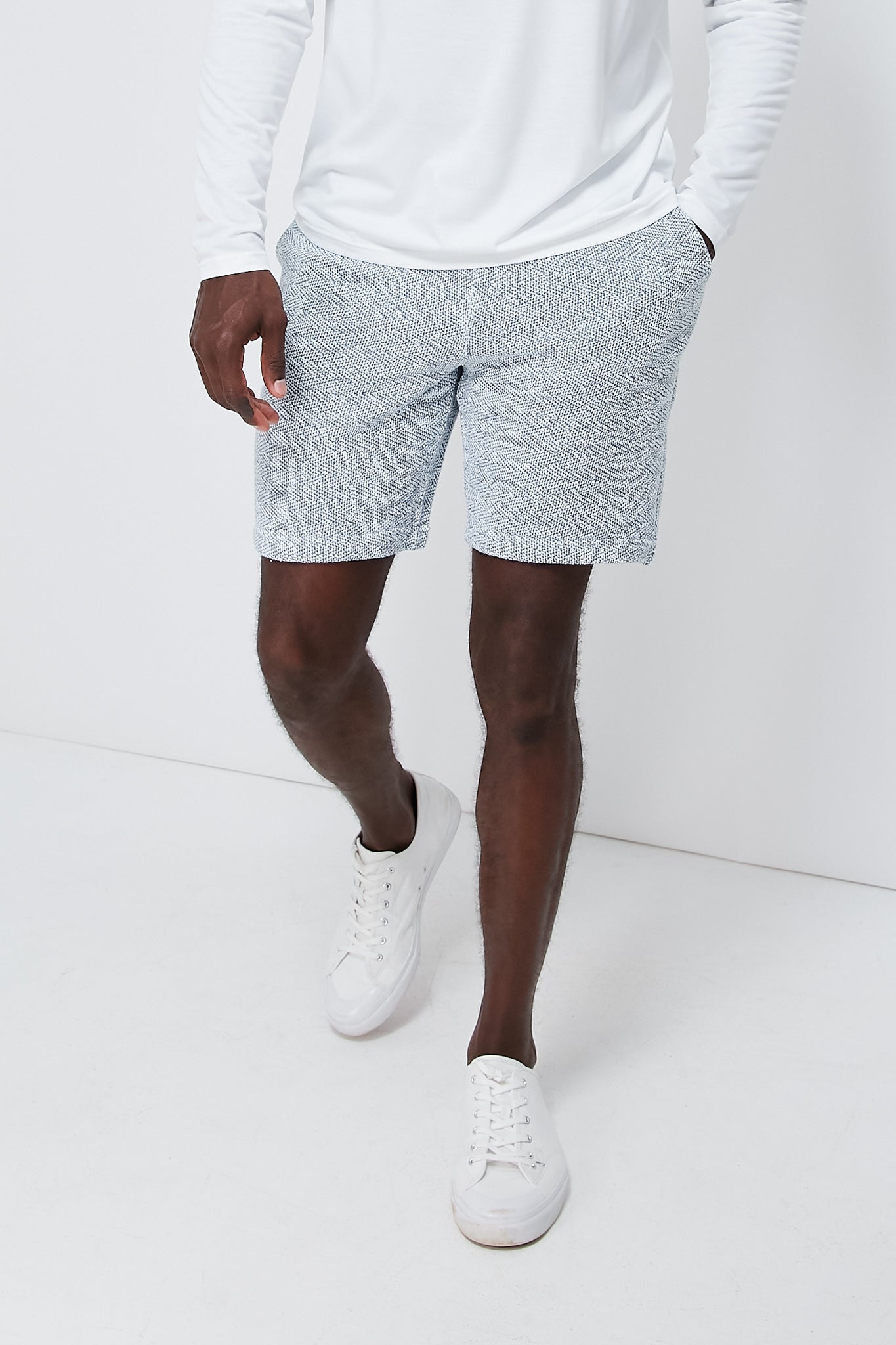 A person in Faherty’s white long-sleeve shirt, lightweight sweatshorts, and white sneakers highlights the brand’s sustainable and comfortable loungewear style.