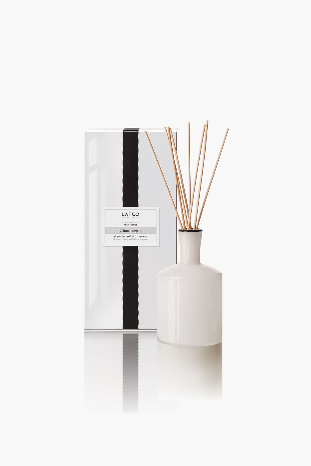 A white ceramic LAFCO New York reed diffuser with essential oils and reed sticks stands next to a white rectangular box with a black vertical stripe and product label.