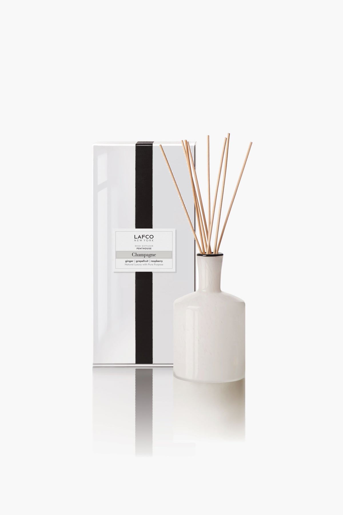 A white ceramic LAFCO New York reed diffuser with essential oils and reed sticks stands next to a white rectangular box with a black vertical stripe and product label.
