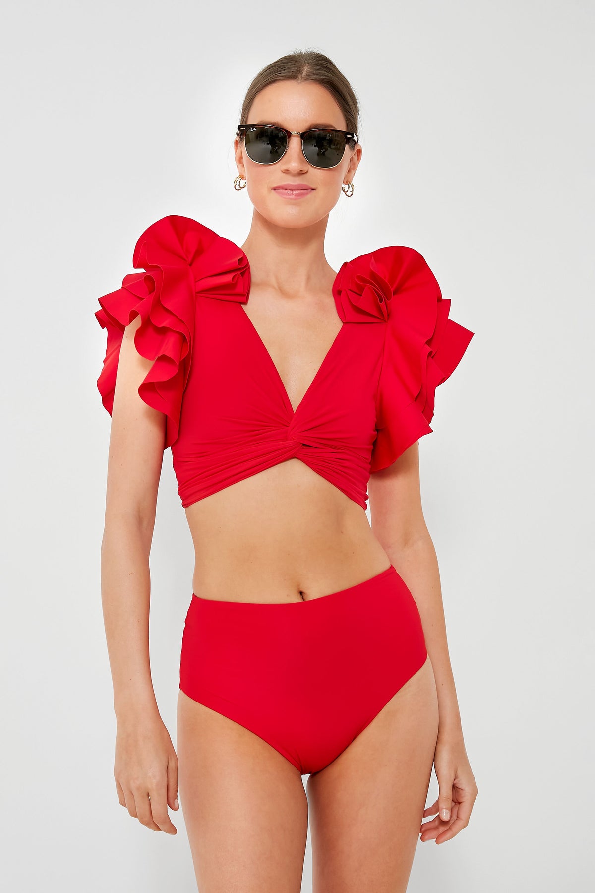 A woman stands confidently in black sunglasses and a bold red Maygel Coronel Kai Two Piece bikini featuring dramatic short ruffled sleeves and high-waisted bottoms.