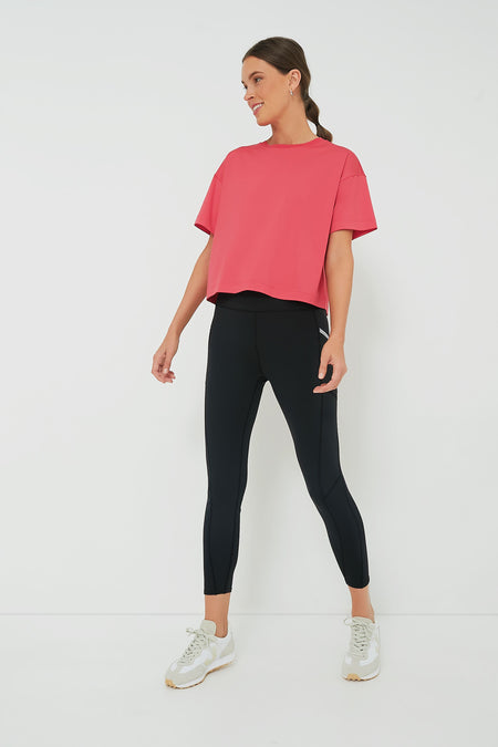 A woman wears a Tnuck Sport pink cropped boyfriend tee with moisture-wicking fabric, black leggings, and white sneakers.