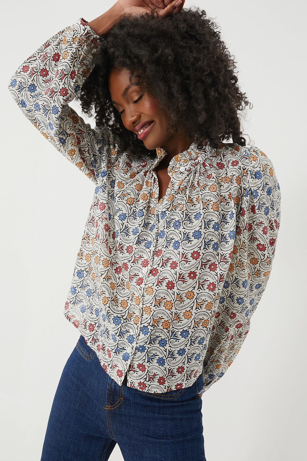 A woman in an Alix of Bohemia hand-block printed blouse and blue jeans poses with one arm raised.