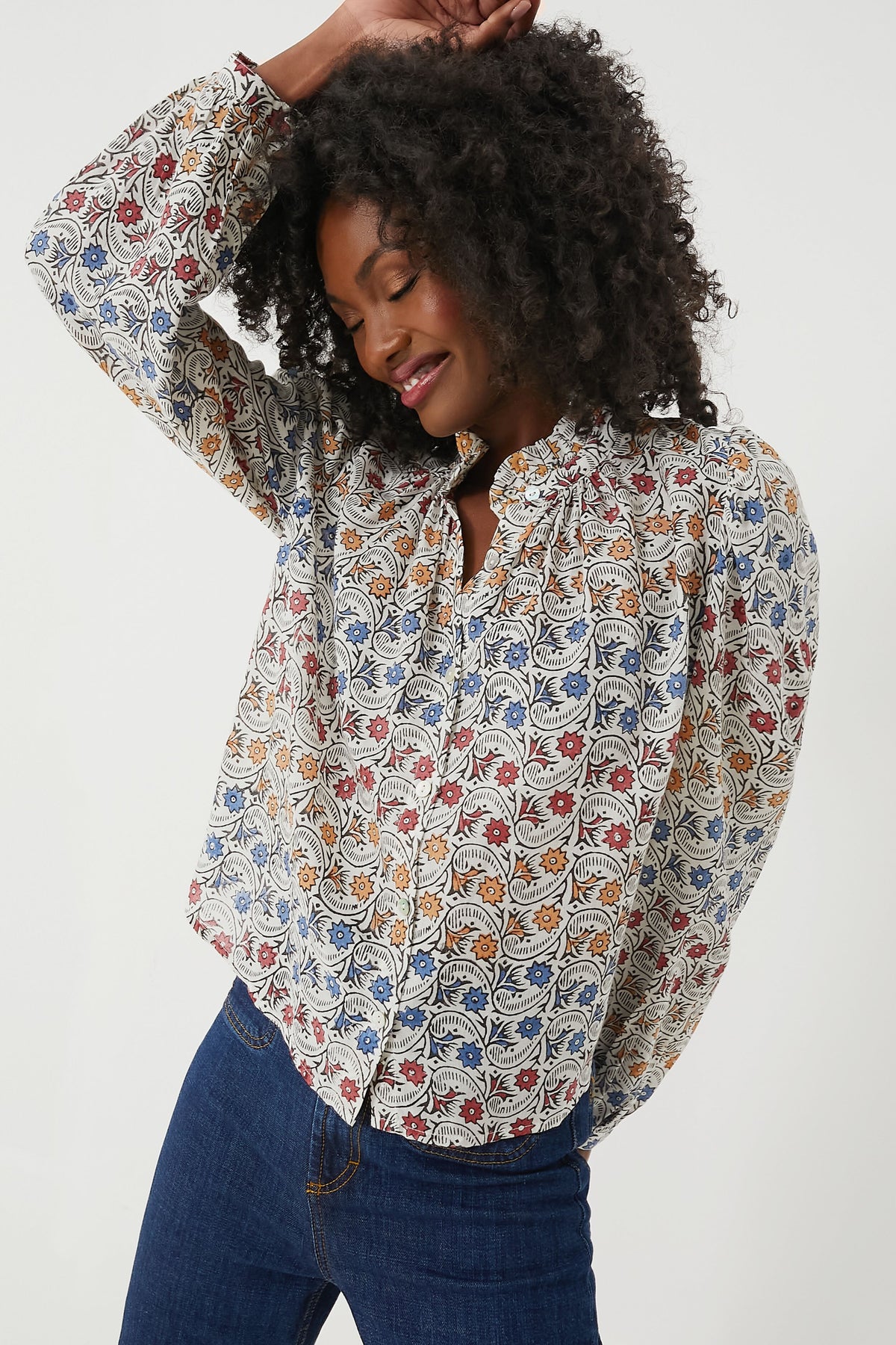 A woman in an Alix of Bohemia hand-block printed blouse and blue jeans poses with one arm raised.