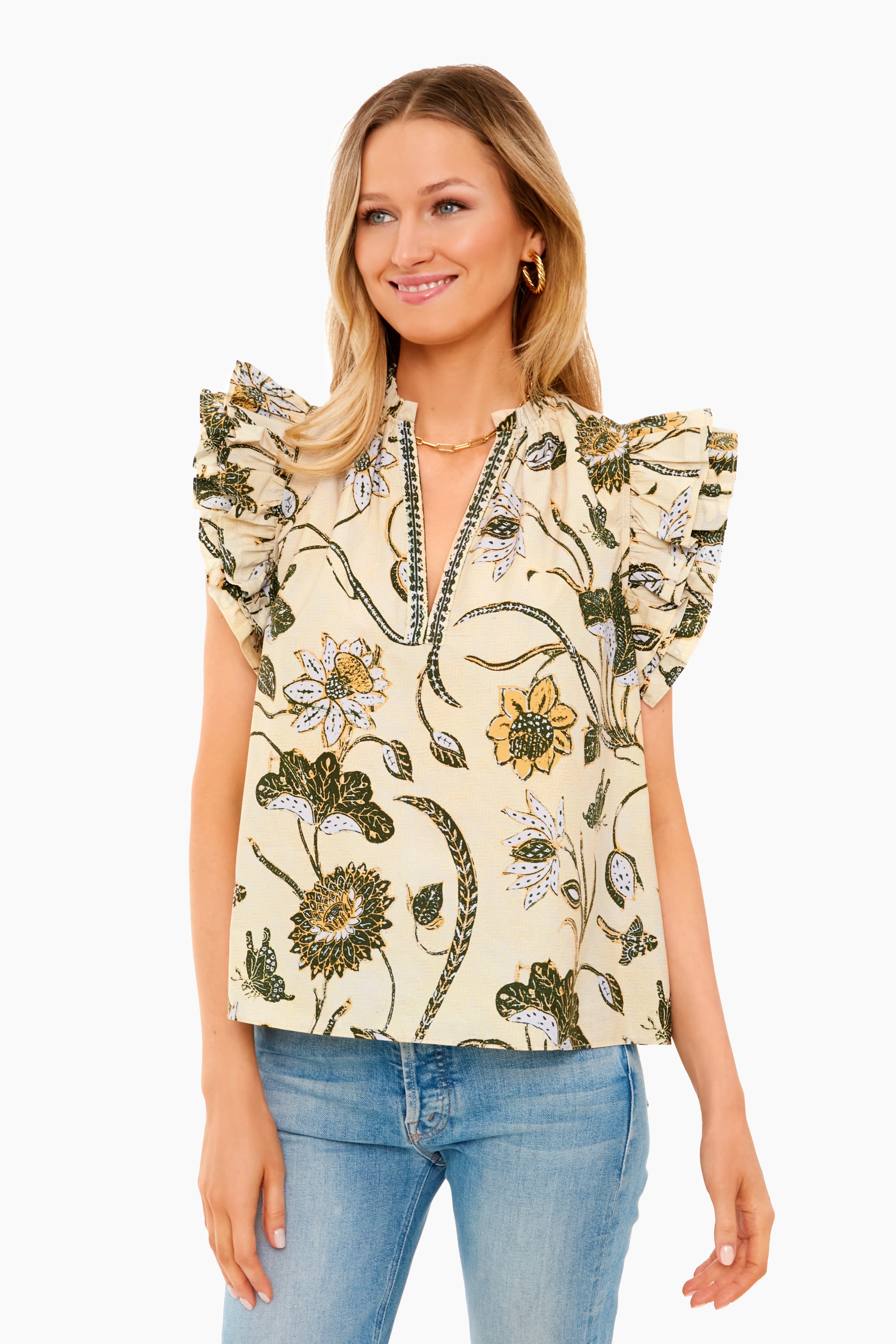 A woman in a Ulla Johnson short-sleeve floral cotton poplin blouse with ruffled shoulders and light blue jeans smiles brightly.