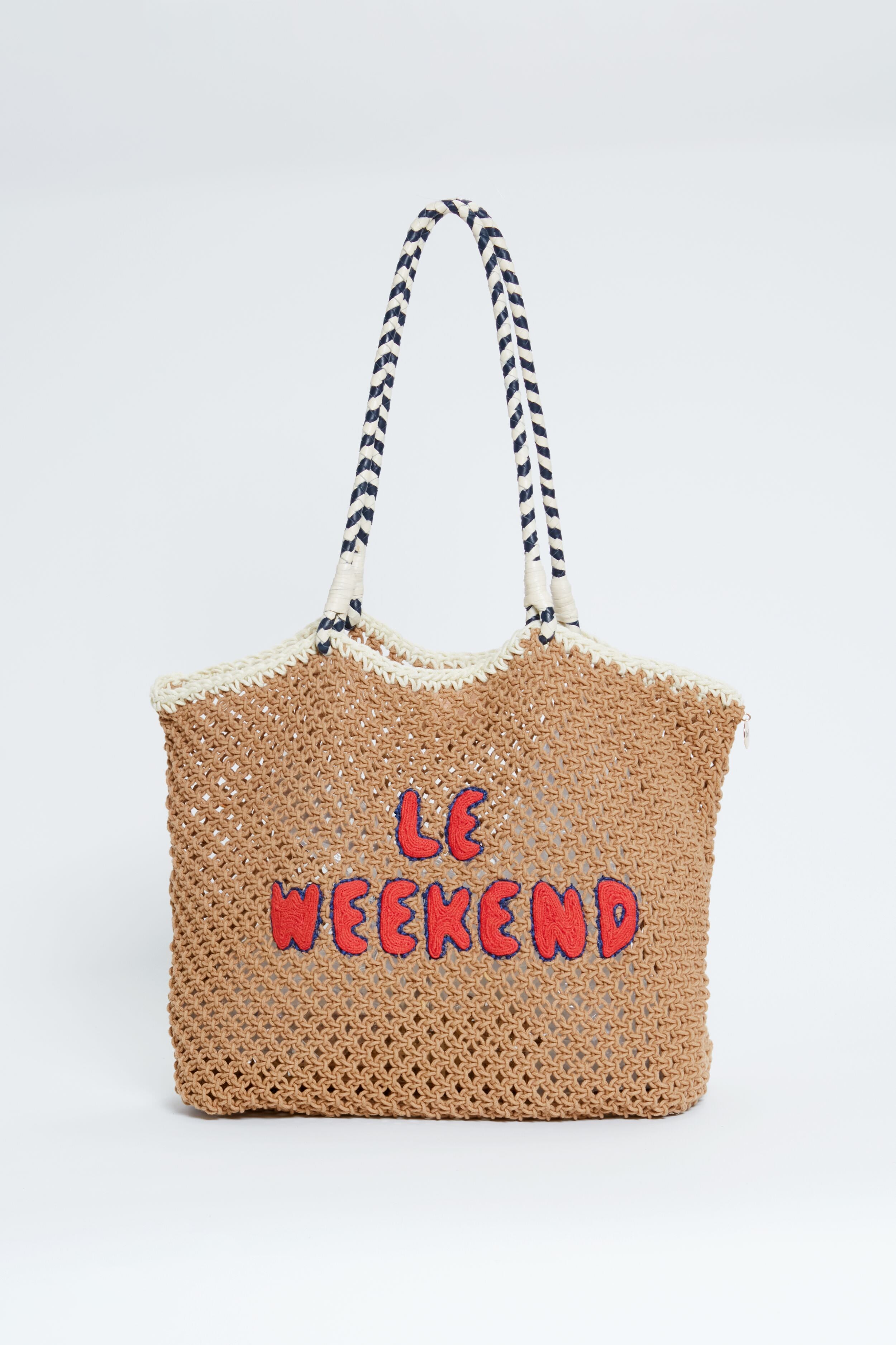 A Clare V woven straw summer bag features black and white striped handles and red "LE WEEKEND" lettering on the front, inspired by the iconic Clare V tote.