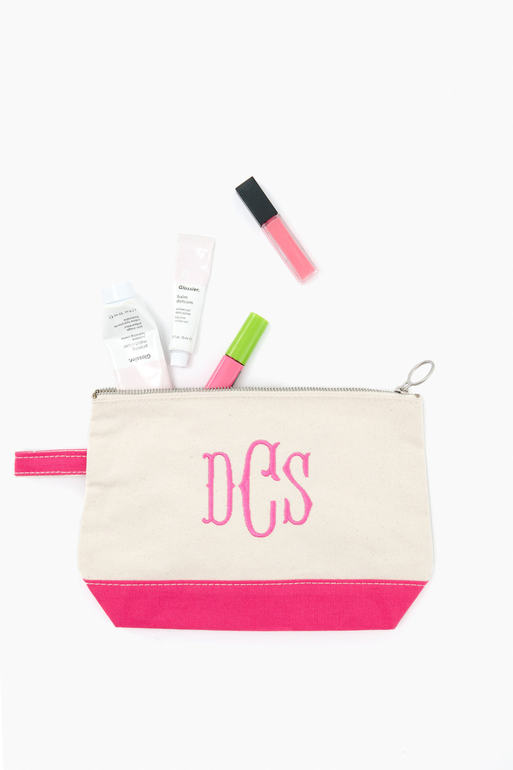 A beige and pink CB Station monogrammed makeup bag with “DCS” neatly holds skincare and makeup items, such as tubes and a lip gloss.