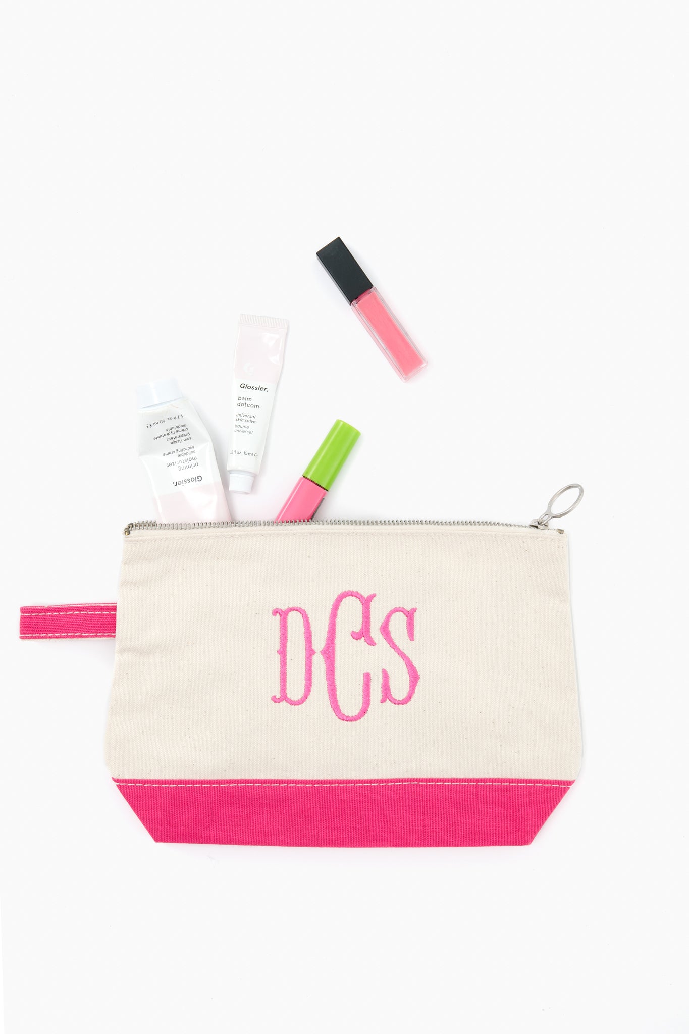 A beige and pink CB Station monogrammed makeup bag with “DCS” neatly holds skincare and makeup items, such as tubes and a lip gloss.