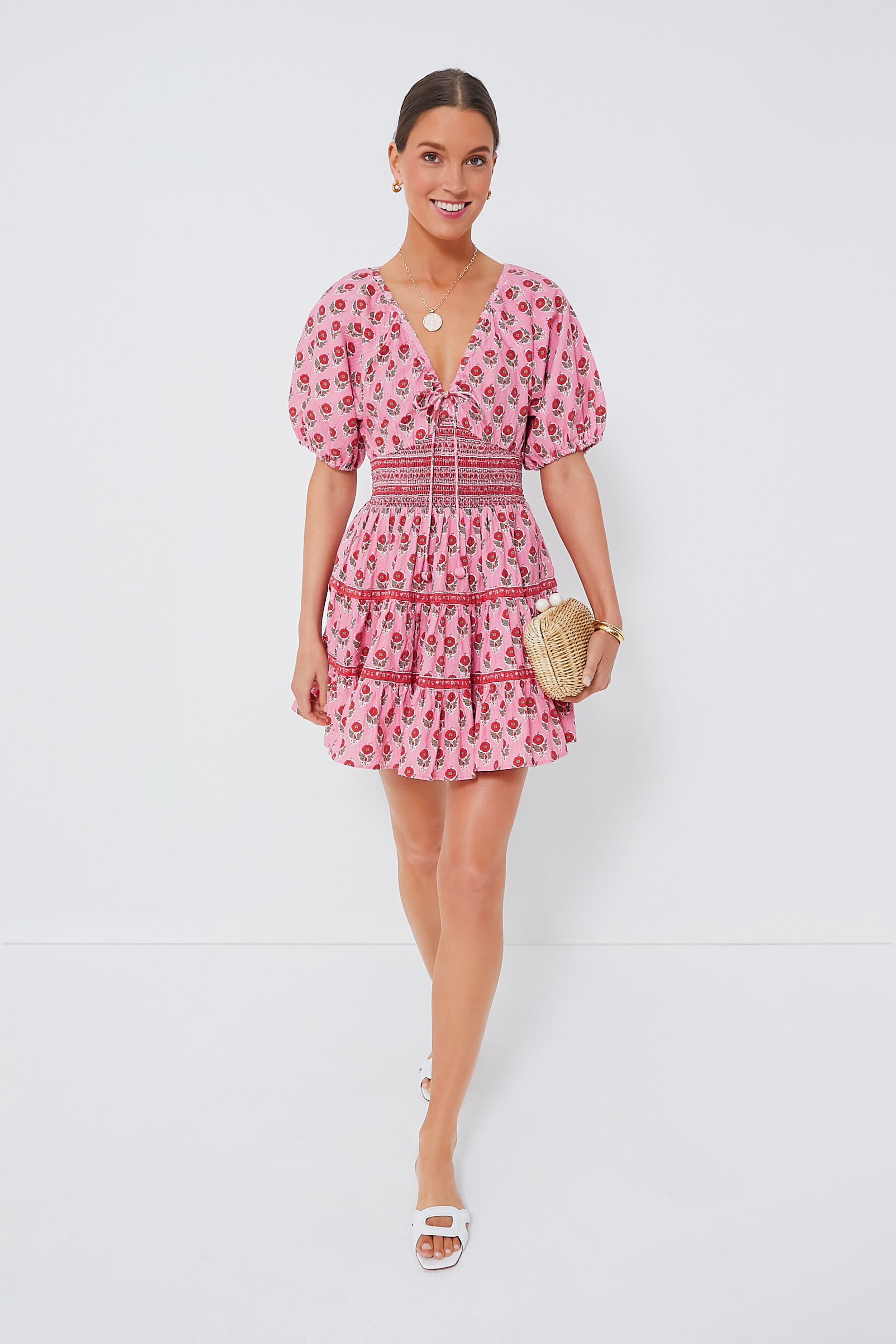 A woman wears a Saylor pink boho-chic mini dress with puffy sleeves, paired with white sandals and a small woven clutch.