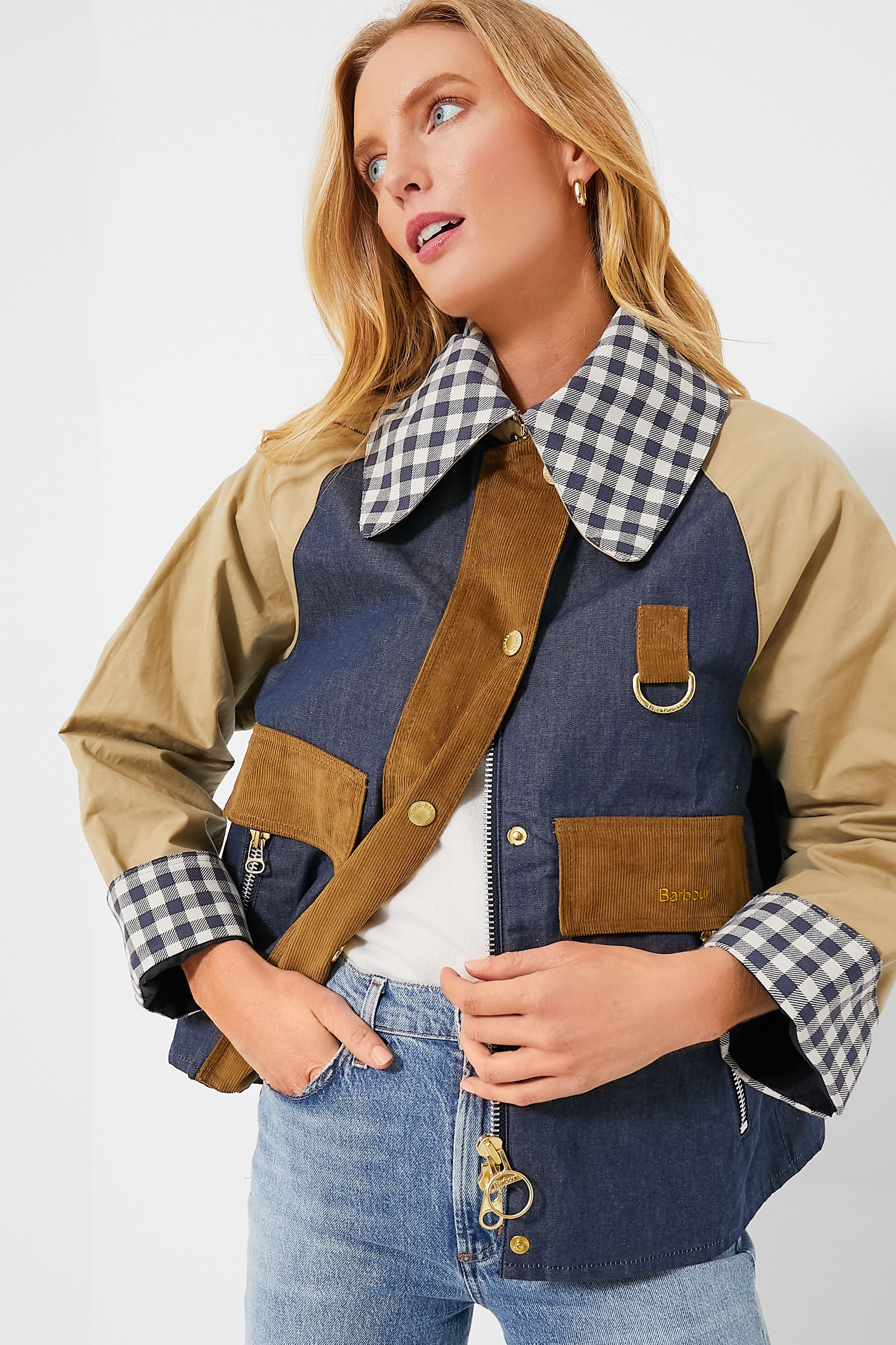 A woman wears a Barbour cropped jacket featuring beige sleeves, a large gingham collar, denim front with pockets and gold hardware, styled with light blue jeans and a white top.