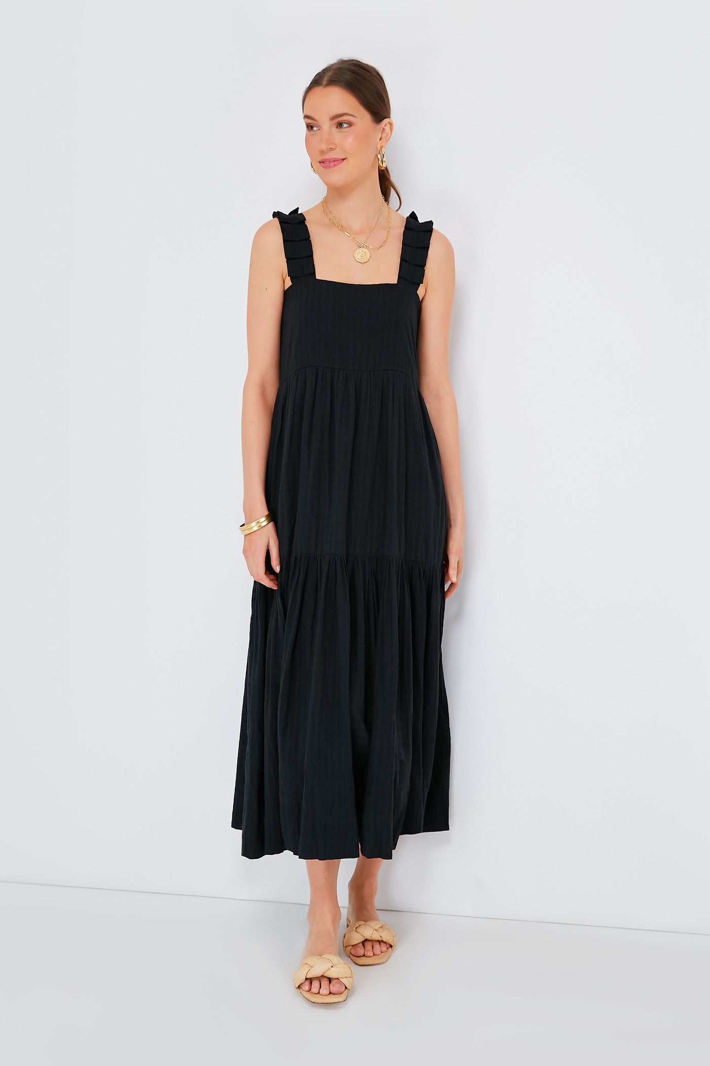 A woman wears MIRTH’s sleeveless, black ankle-length artisan dress with ruffled straps, paired with gold jewelry and beige sandals—an elegant example of ethical resortwear.