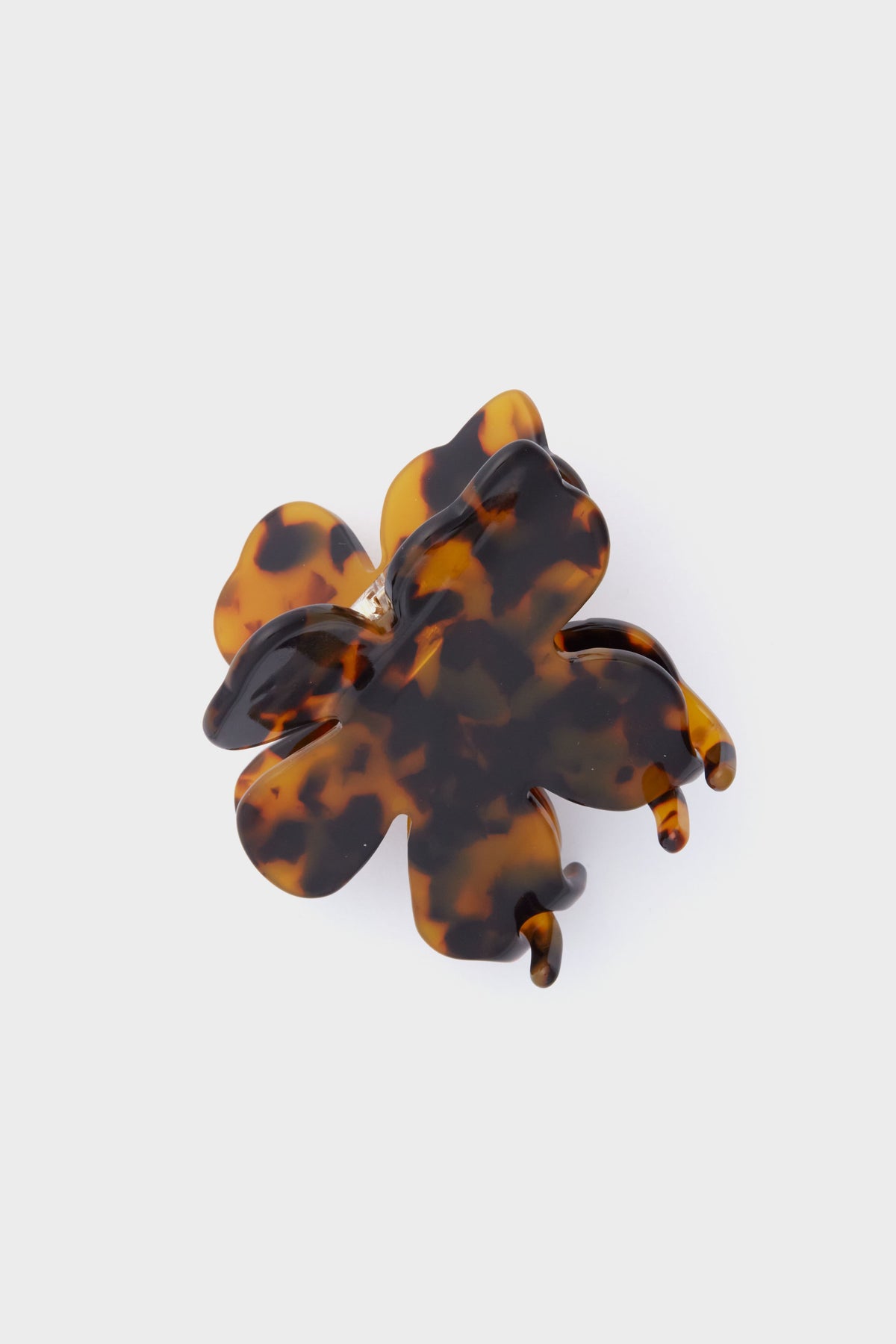 A Lele Sadoughi flower-shaped hair clip in brown and black tortoise is shown, offering a stylish floral accessory for your hair.