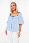 A woman wears a Pomander Place Celia Top with sky blue stripes, a square neckline, and short flared sleeves, styled with white pants.