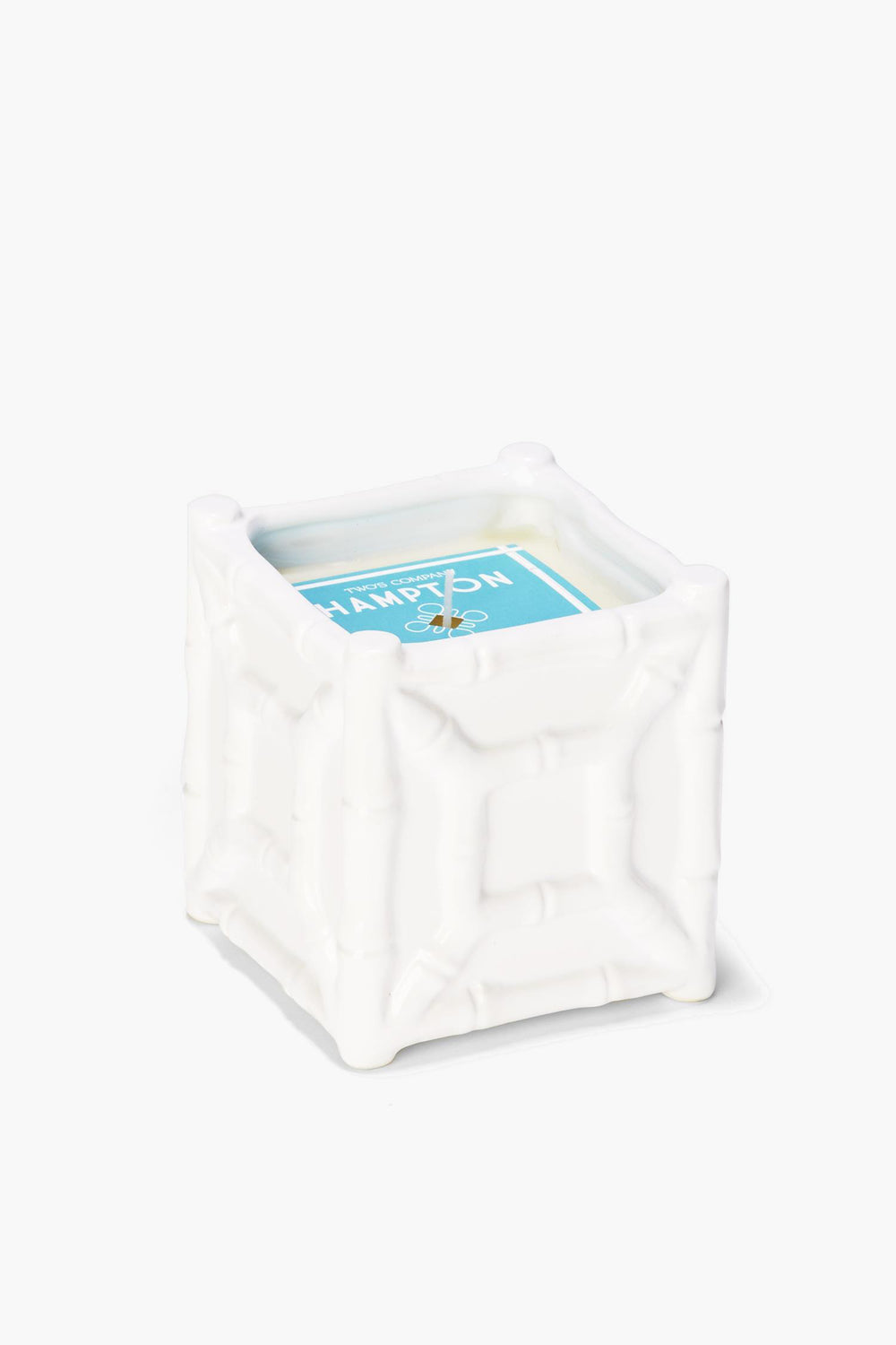 A white, square bamboo candle holder by Two's Company with a textured chinoiserie design, featuring a sea spray scent candle with a blue label.