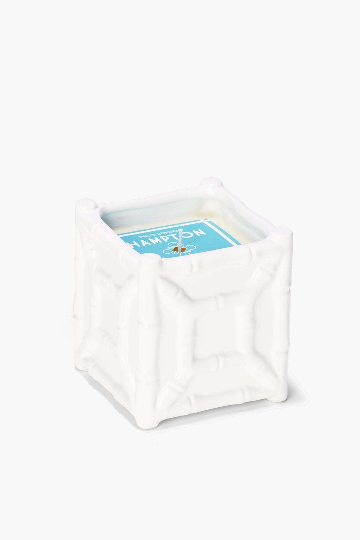 A white, square bamboo candle holder by Two's Company with a textured chinoiserie design, featuring a sea spray scent candle with a blue label.
