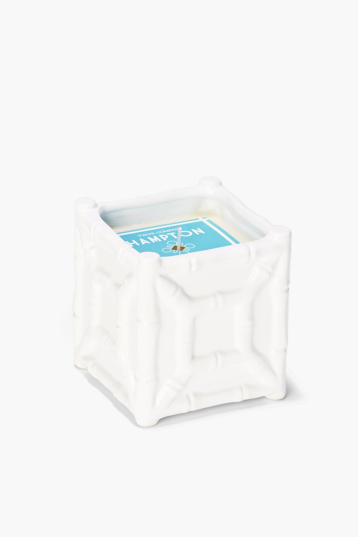 A white, square bamboo candle holder by Two's Company with a textured chinoiserie design, featuring a sea spray scent candle with a blue label.